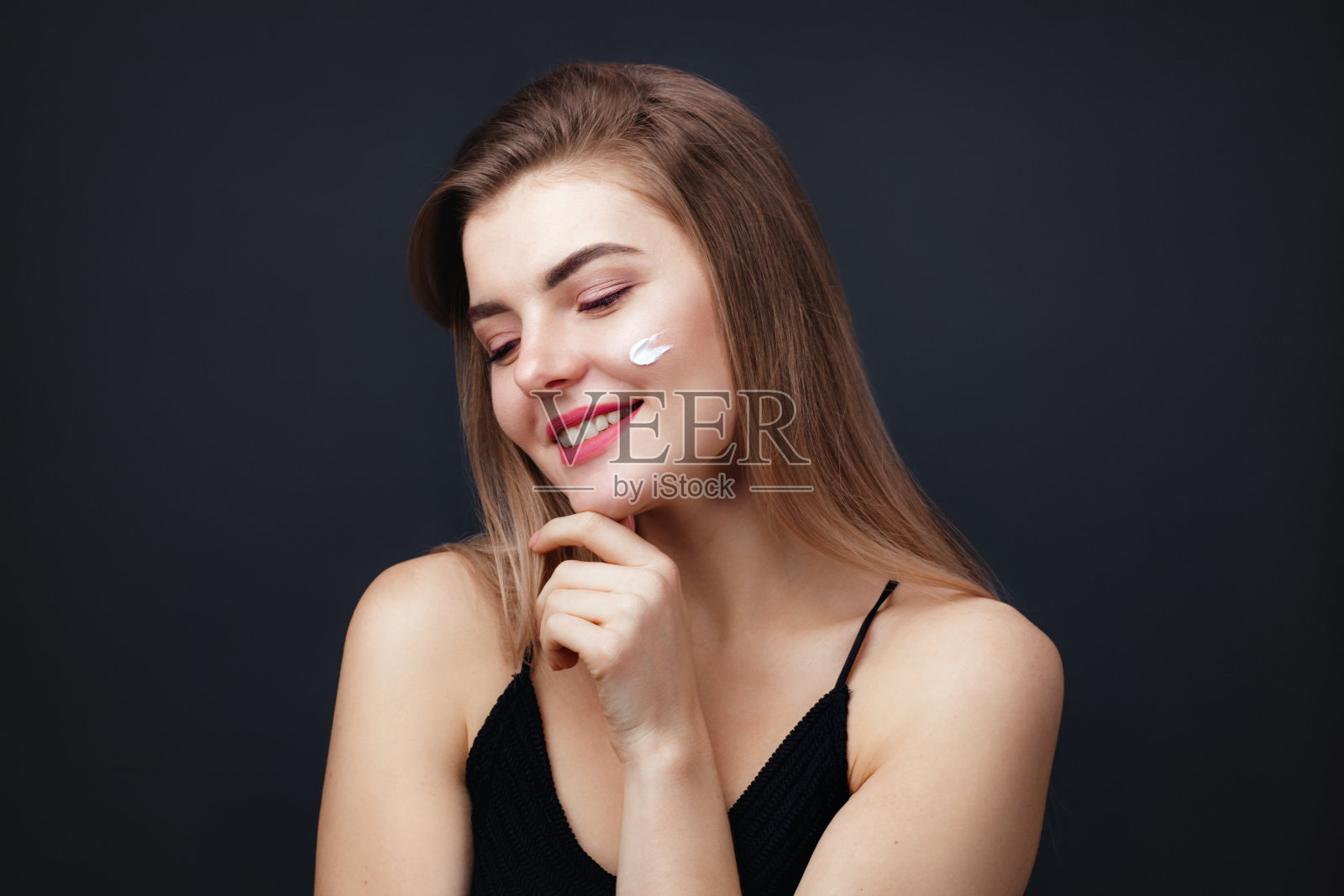 拥有健康肌肤的漂亮女人在脸上涂抹护肤霜照片摄影图片