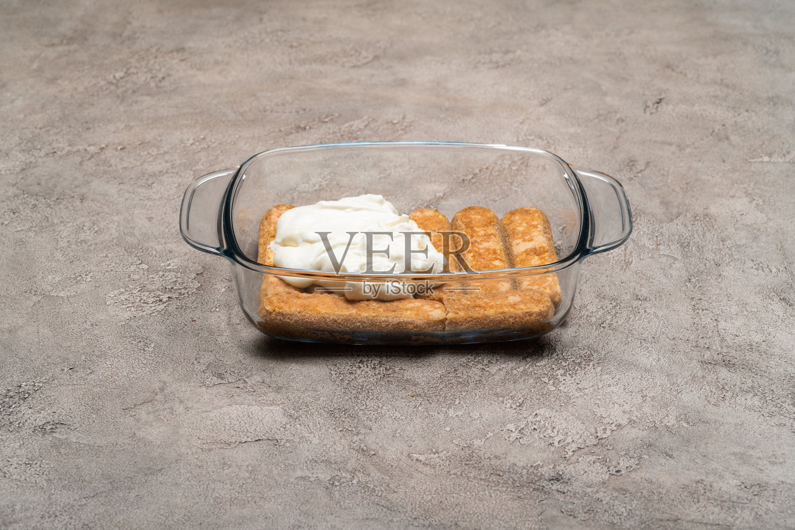 提拉米苏甜点烹饪-传统的意大利Savoiardi手指饼干和奶油在玻璃烤盘的混凝土背景照片摄影图片