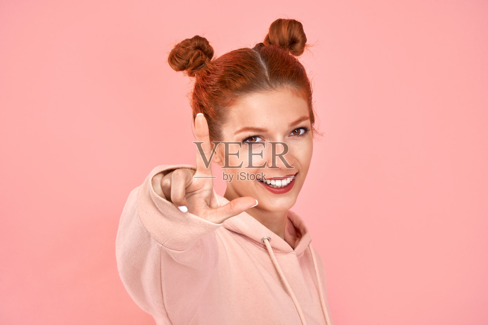 年轻女子在粉色背景上伸出一根手指，表示计数照片摄影图片