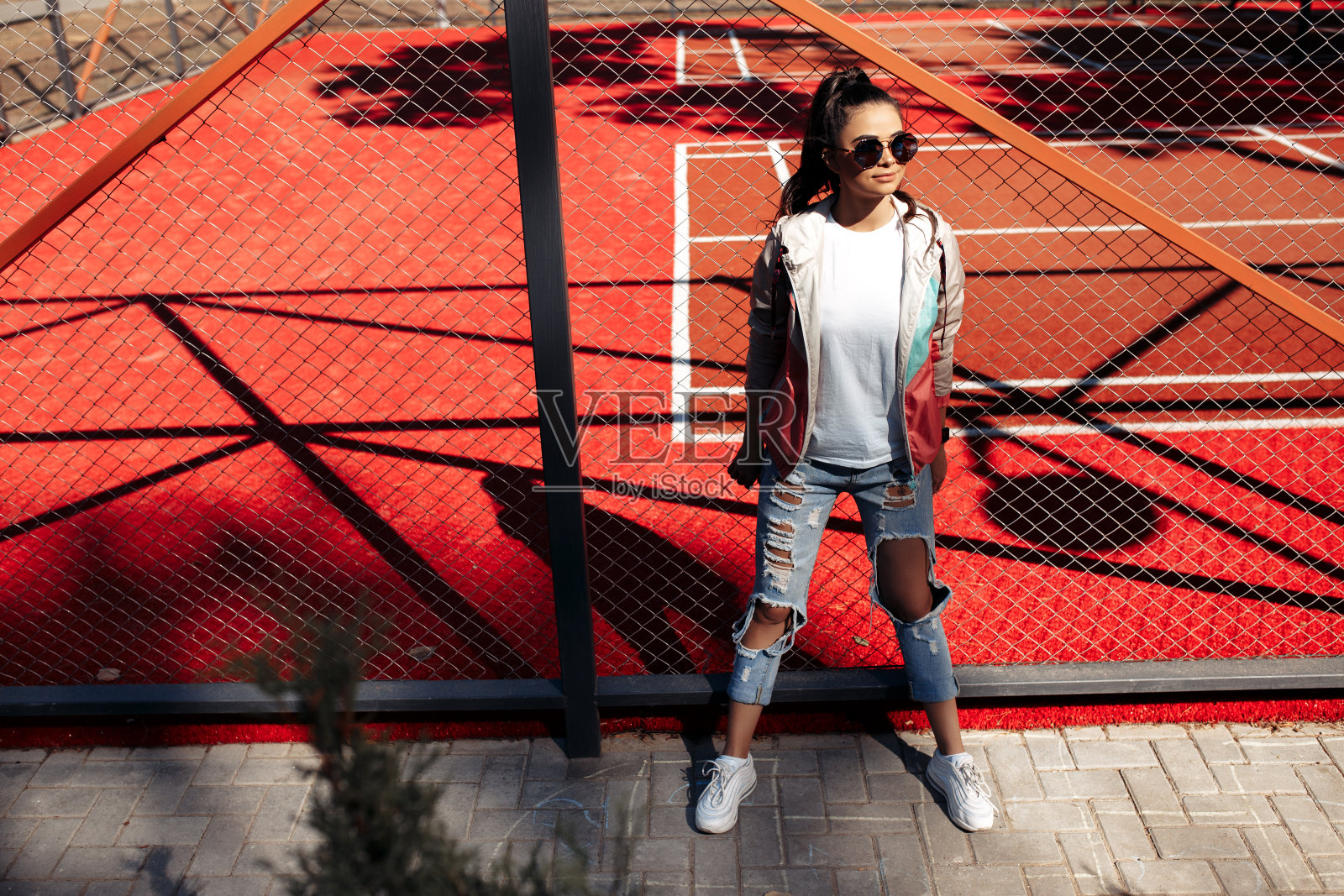 时髦的黑发年轻女子与明亮的笑容穿着休闲现代服装摆姿势在体育场。照片摄影图片