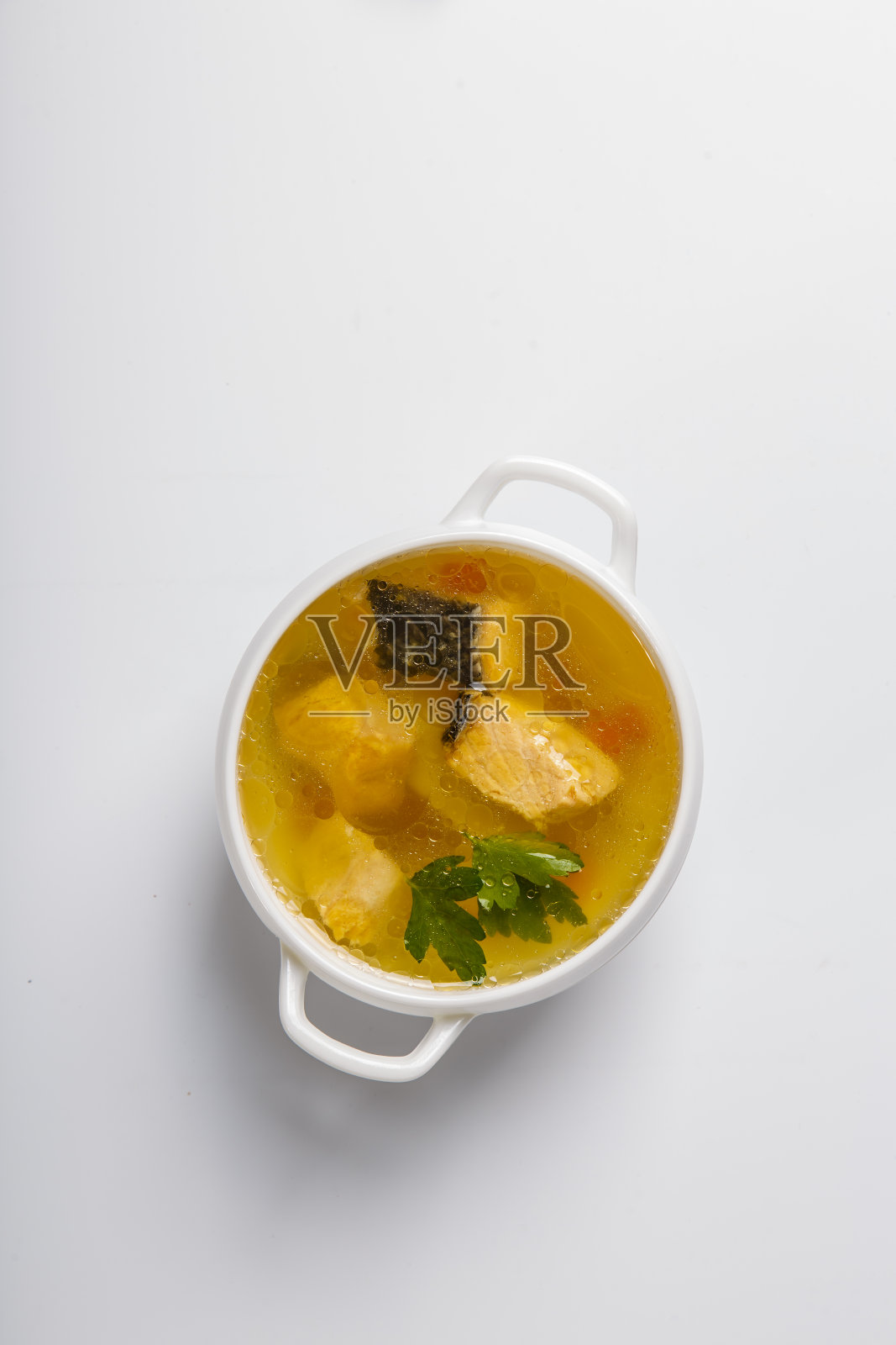 三文鱼鱼汤。一个白色的圆形盘子里盛着透明的肉汤，上面有三文鱼、土豆和绿色蔬菜。白色背景上的盘子。从上往下看照片摄影图片