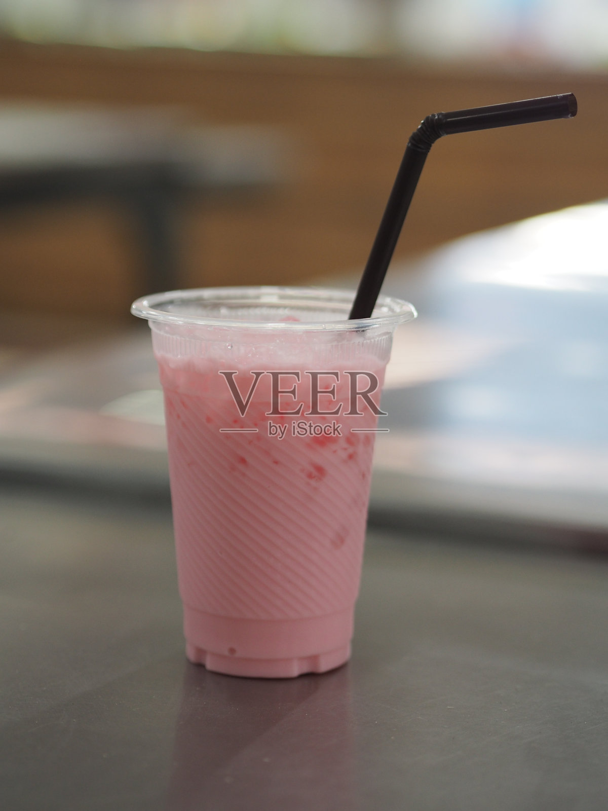 用透明的塑料杯装着冰冻的粉色牛奶，桌上放着棕色的塑料管照片摄影图片