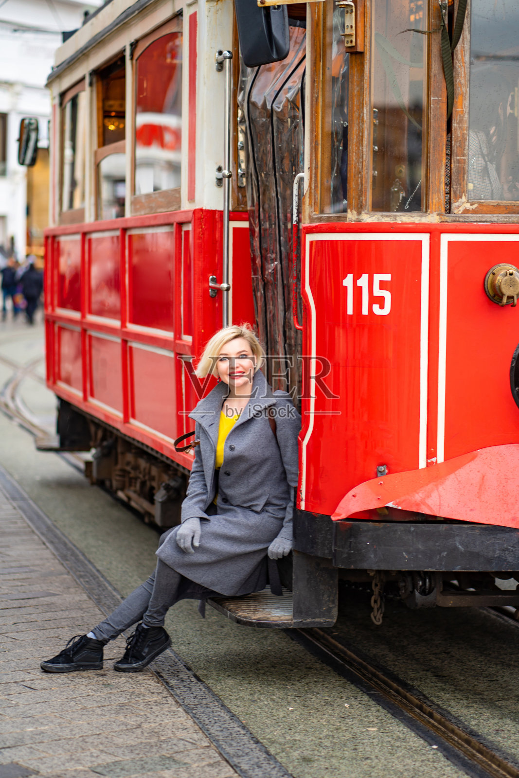 坐在红色有轨电车上的穿外套的金发女孩照片摄影图片