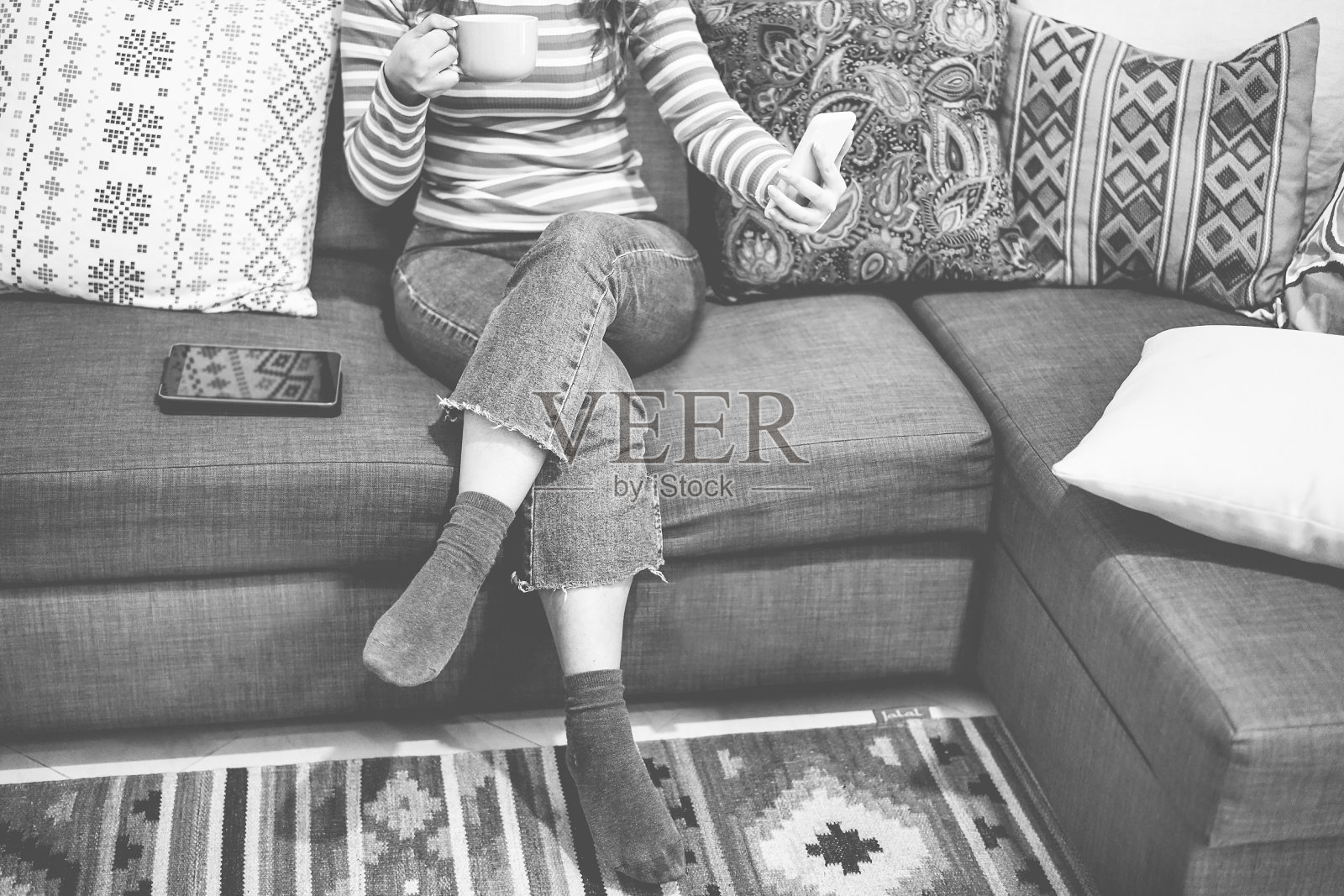 年轻女人在沙发上喝咖啡玩手机 - 女孩的上午休息时间 - 复古时尚概念 - 专注于脚 - 黑白编辑照片摄影图片