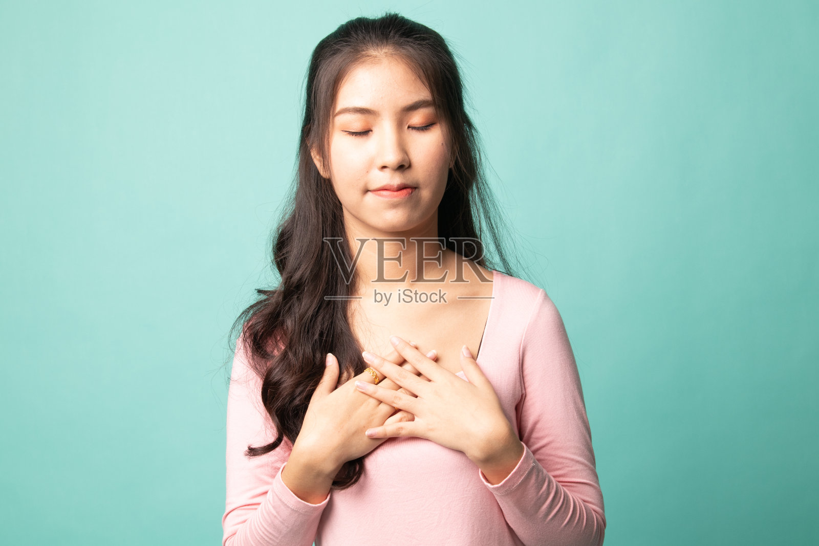 忠实的女人闭上眼睛，把手放在靠近心脏的胸口，表示她的善良。照片摄影图片