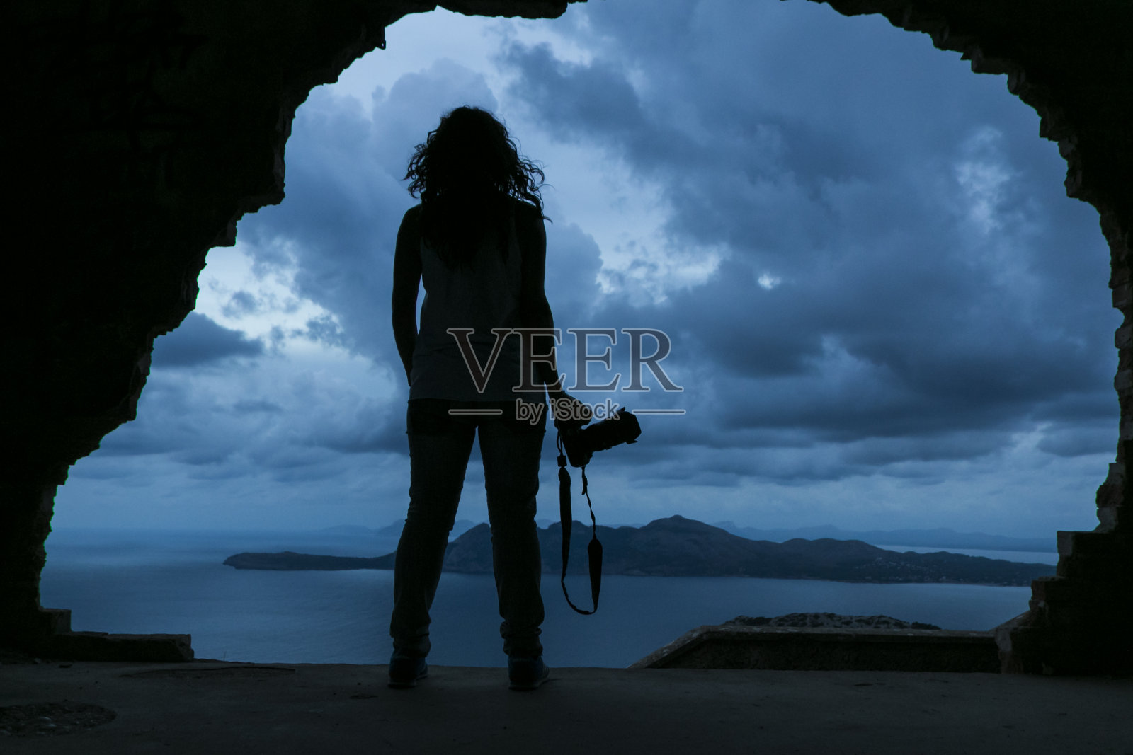 海边岩石上手持相机的年轻女子剪影照片摄影图片