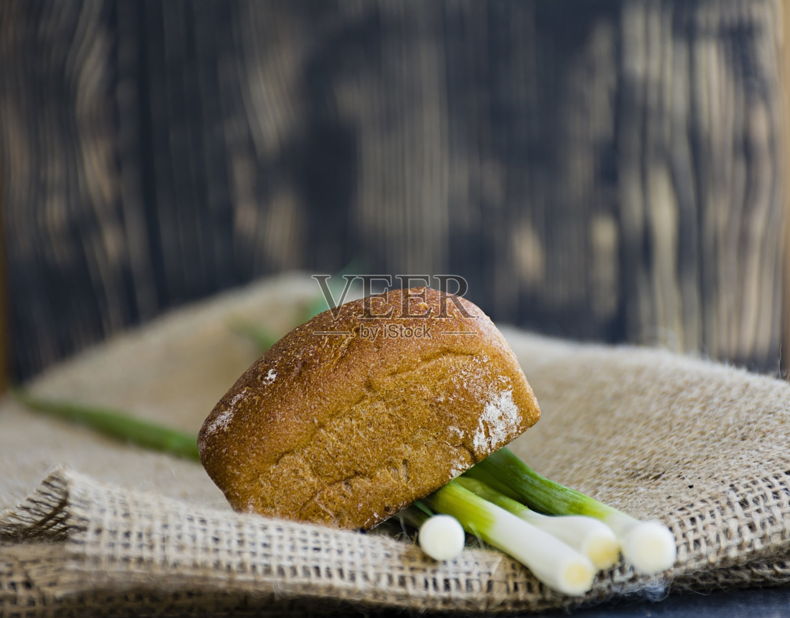 深色木质背景上是新鲜出炉的面包和青葱。照片摄影图片