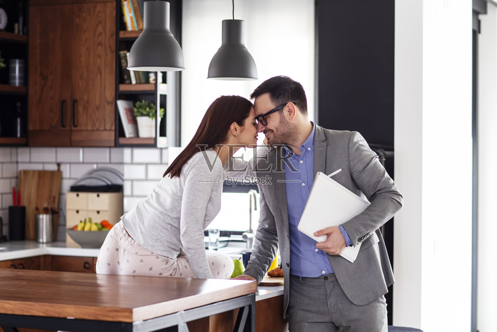 清晨厨房里的现代夫妇：妻子穿着睡衣亲吻即将上班的丈夫照片摄影图片