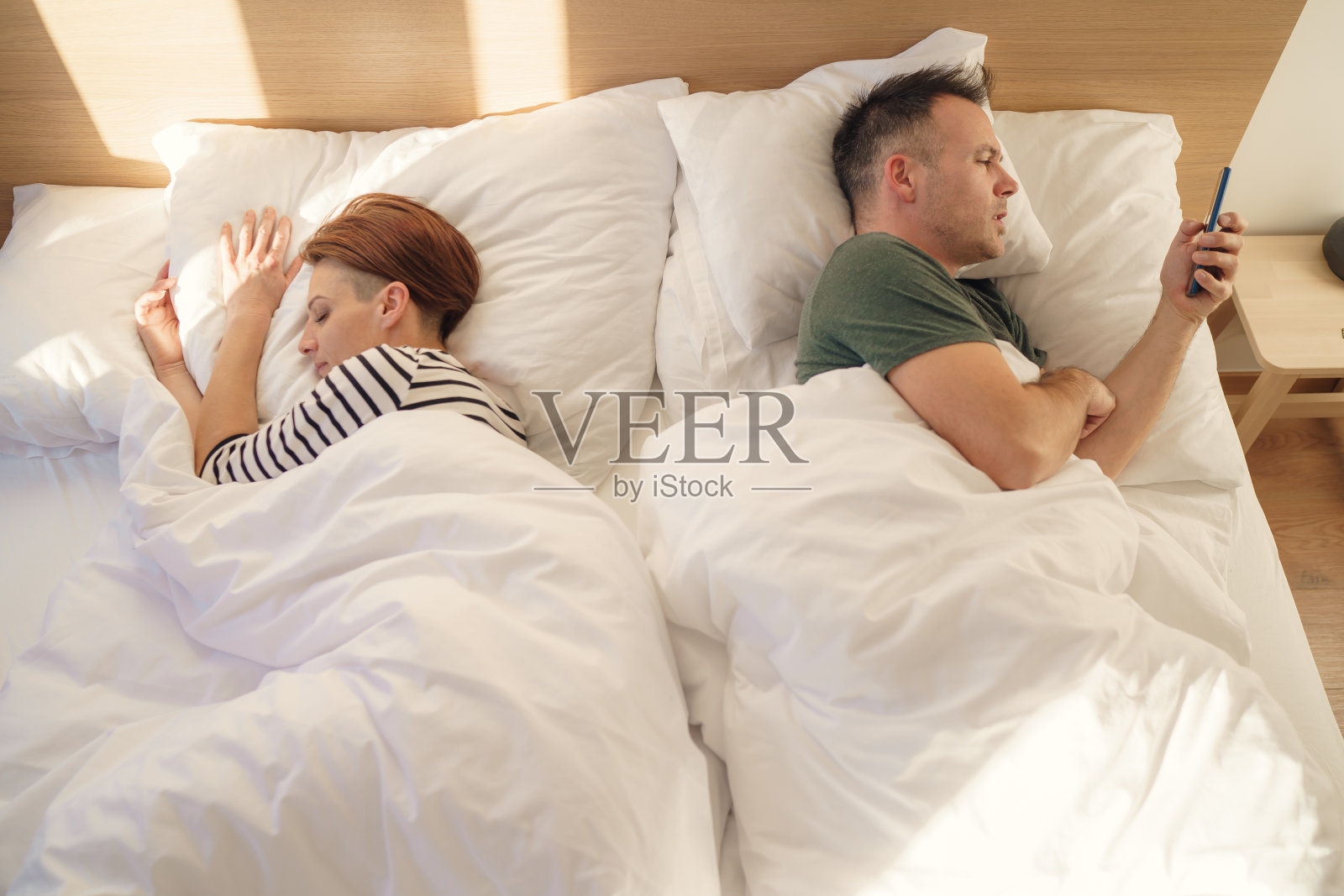 狡猾的男人在床上使用手机，女友正在睡觉照片摄影图片