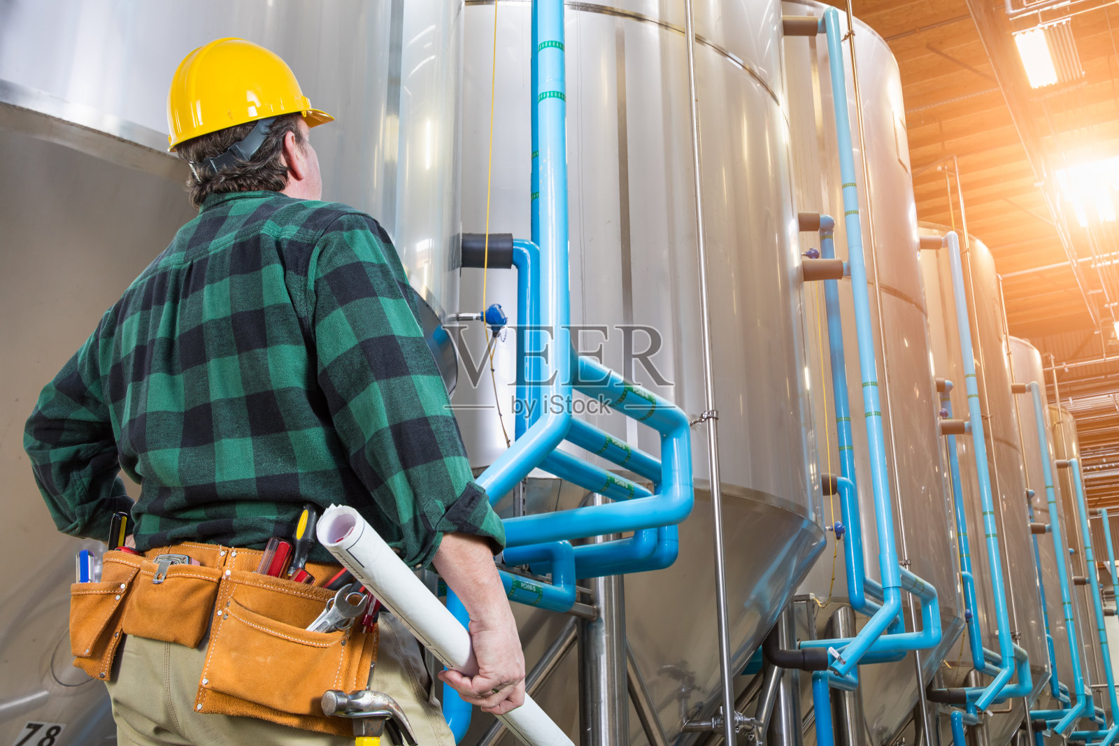 戴着安全帽抬头看大型工业坦克的男人照片摄影图片