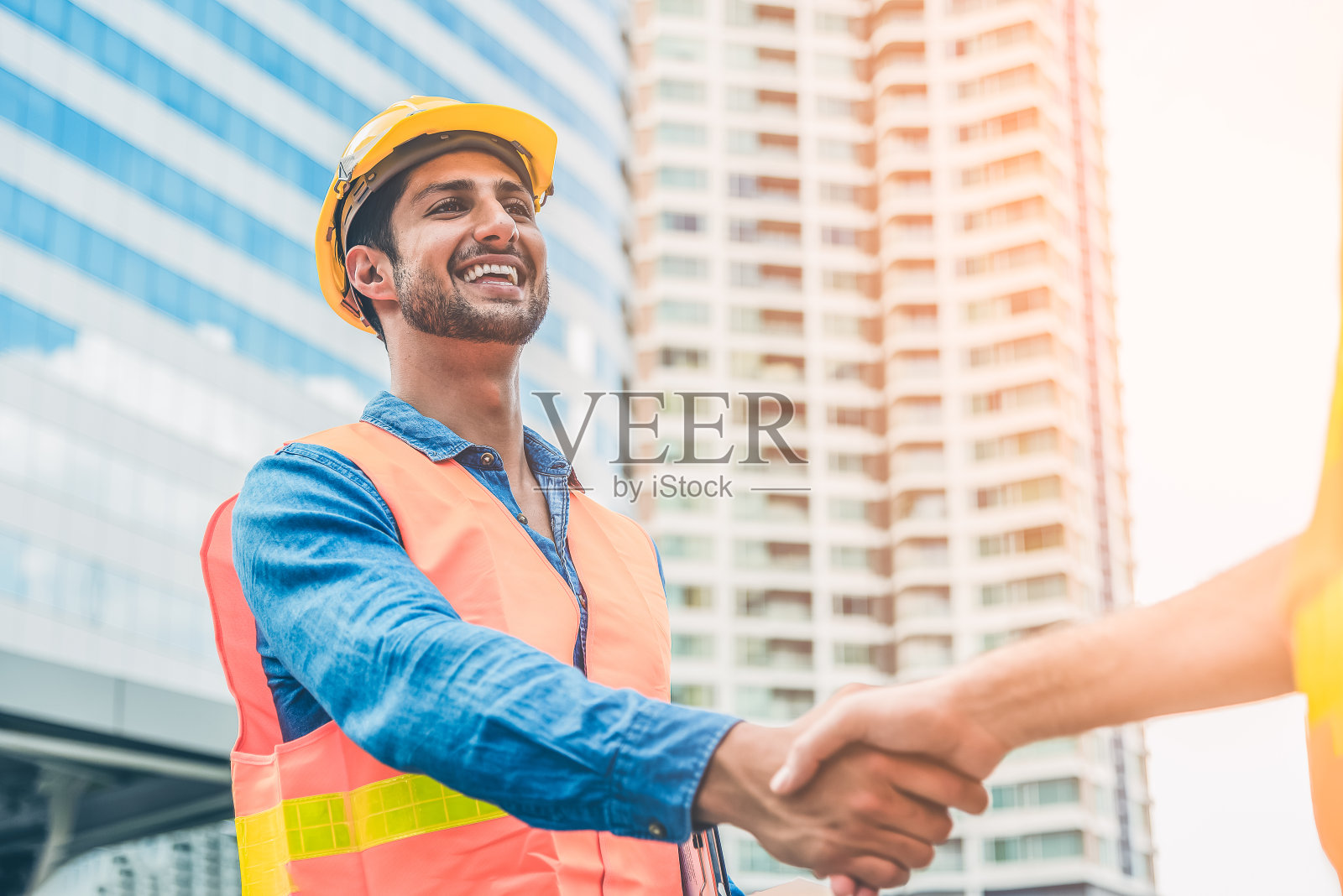 戴黄色头盔的工程师与来访的经理握手问好。现代建筑工程概念。生产和建筑工地的工作安全。照片摄影图片