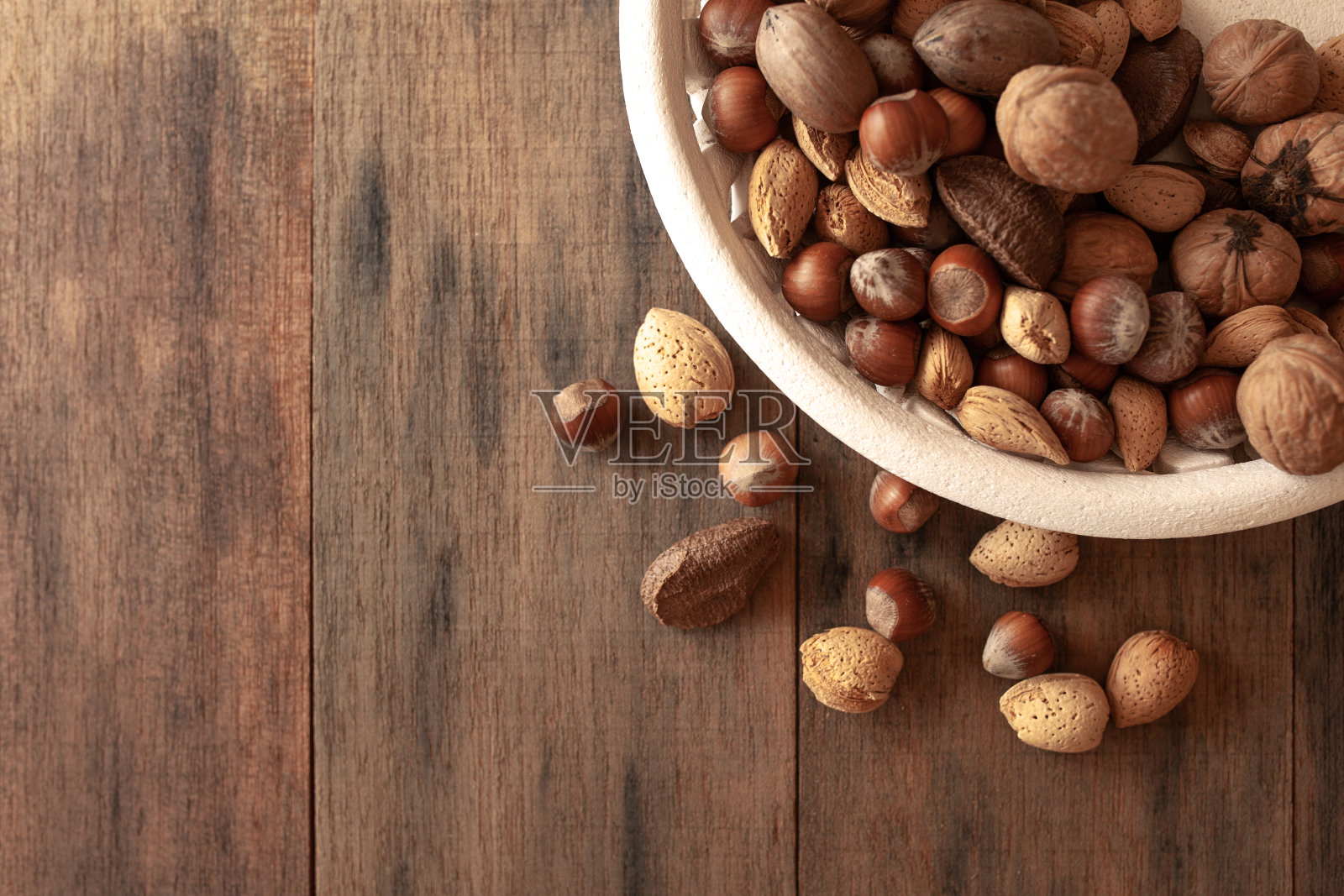 白色盘子和棕色木制背景的什锦坚果照片摄影图片