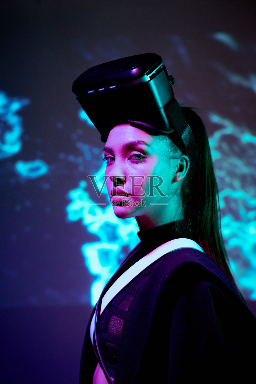 严肃自信的女孩的肖像在VR眼镜的头上站在霓虹灯数字背景照片摄影图片
