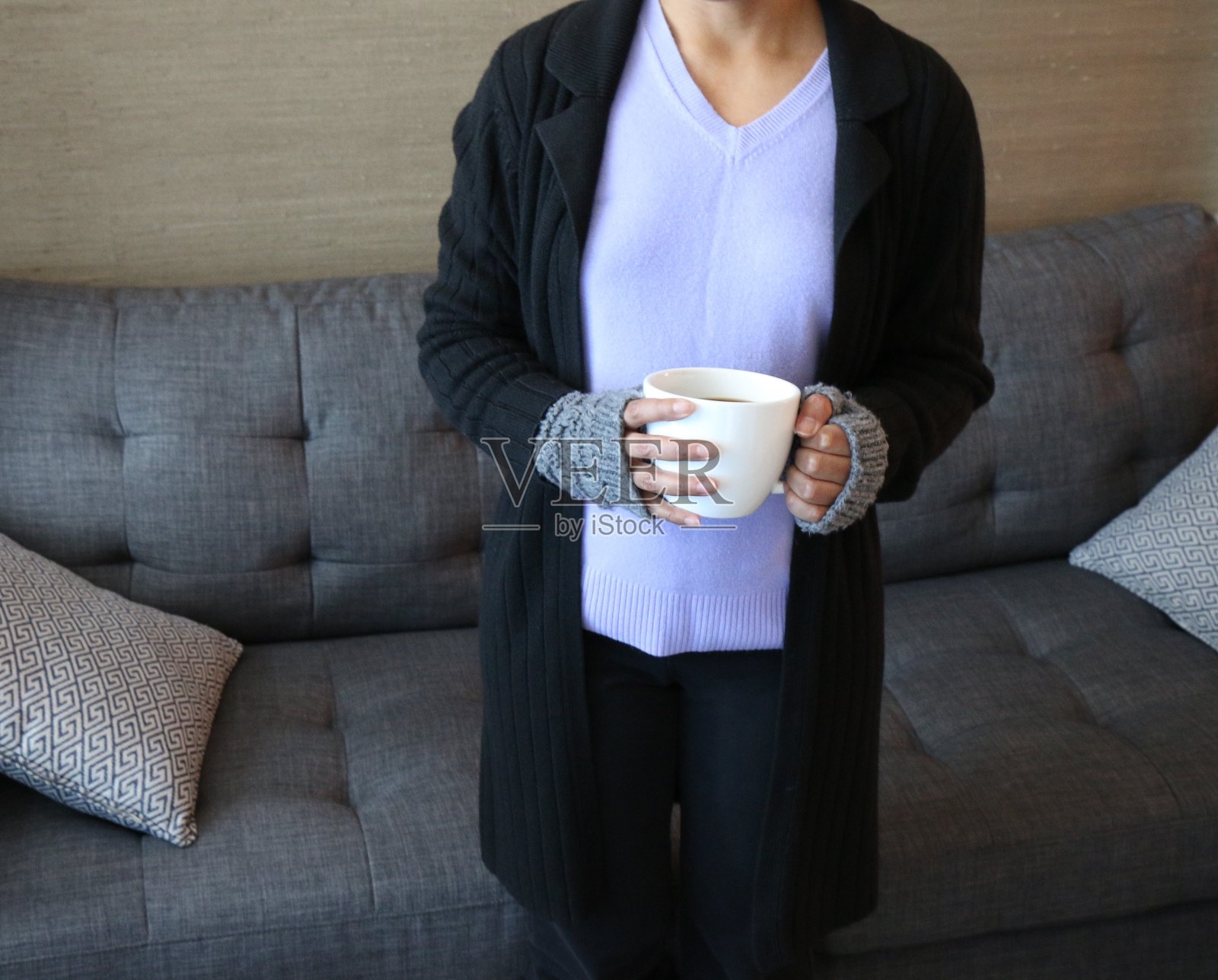 一个女人拿着咖啡杯或茶杯，戴着无指手套，站在客厅里照片摄影图片