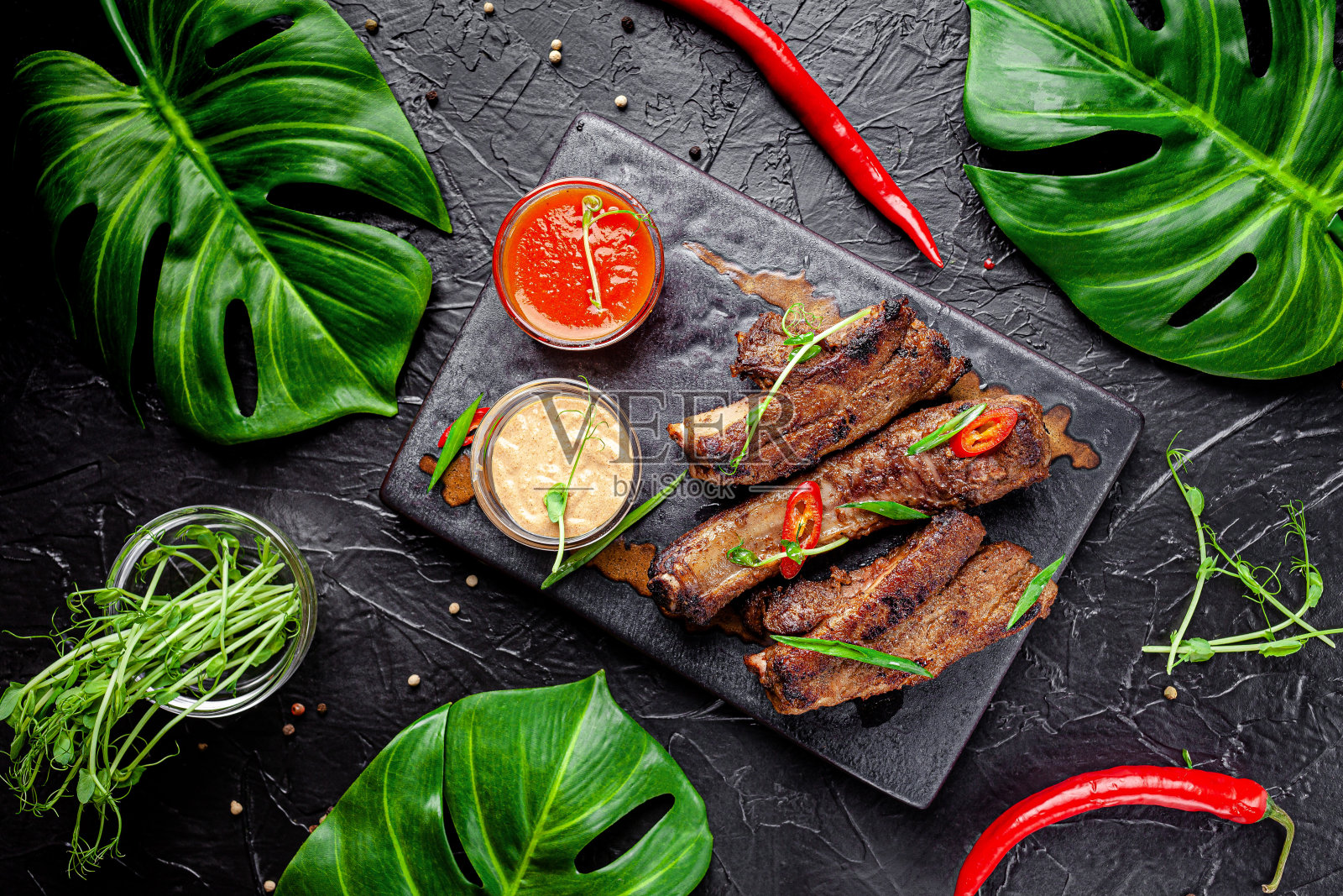 墨西哥菜。烤排骨配辣椒、白汁和红汁。在餐馆里用黑色盘子上菜。背景图像，复制空间文本照片摄影图片