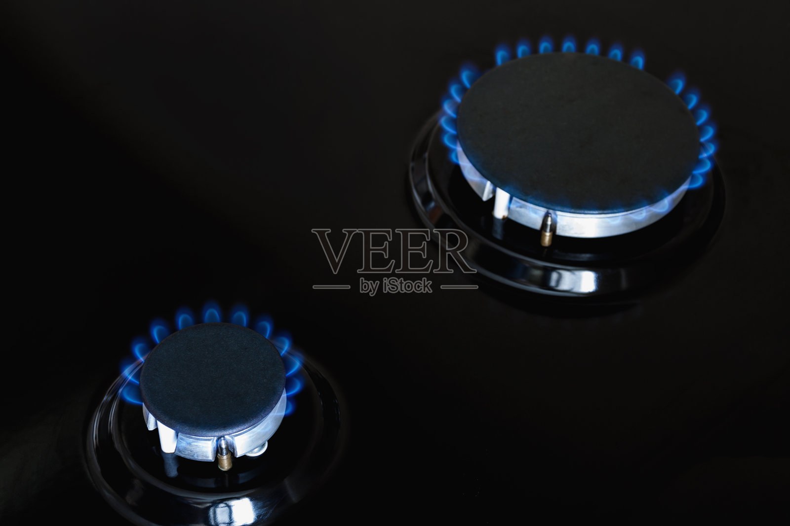 两个煤气炉在黑暗的炉子上燃烧着蓝色的煤气。特写镜头,有选择性的重点照片摄影图片