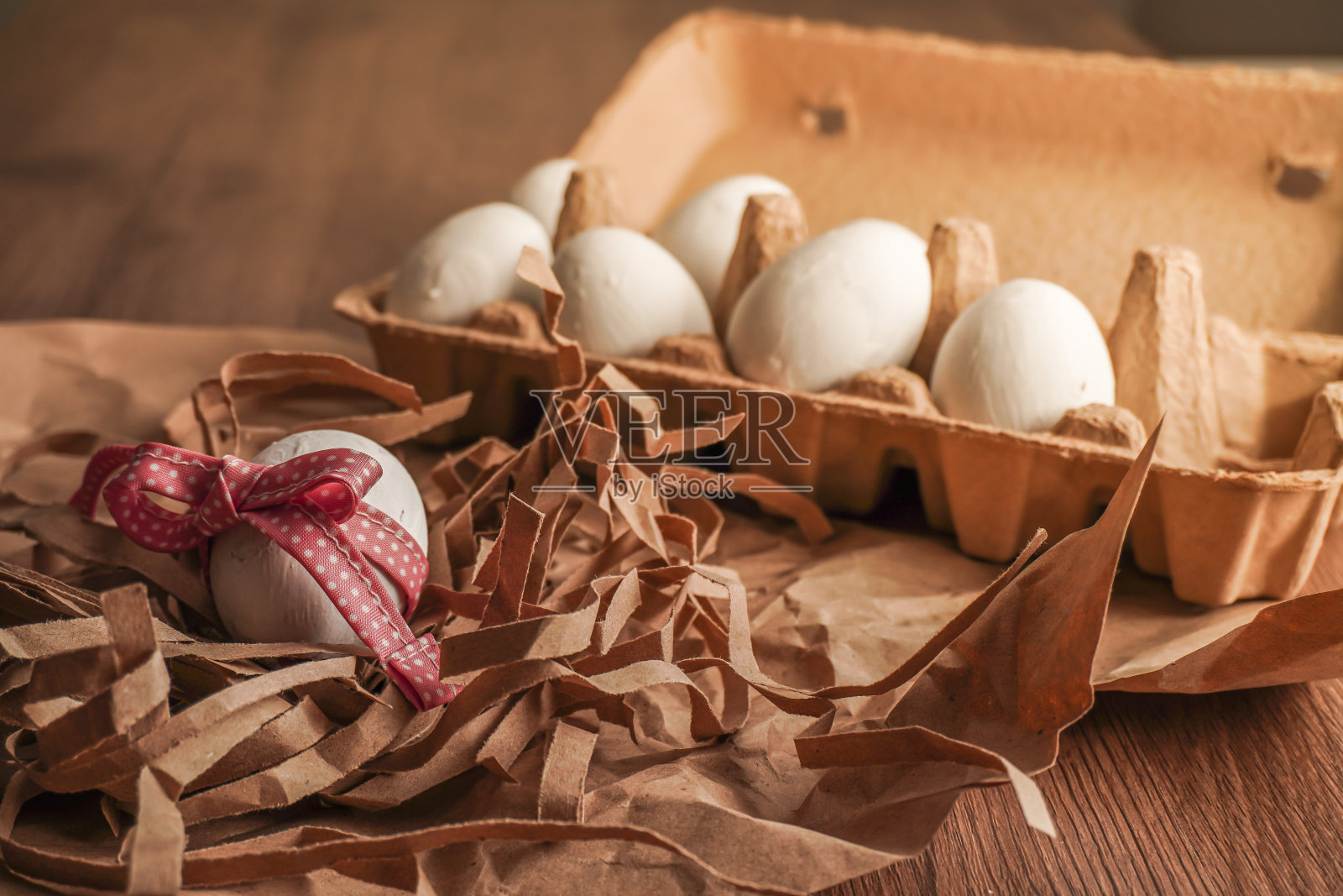 复活节，用红丝带把鸡蛋系好，用牛皮纸把白鸡蛋放在蛋盘上，放在木桌上照片摄影图片