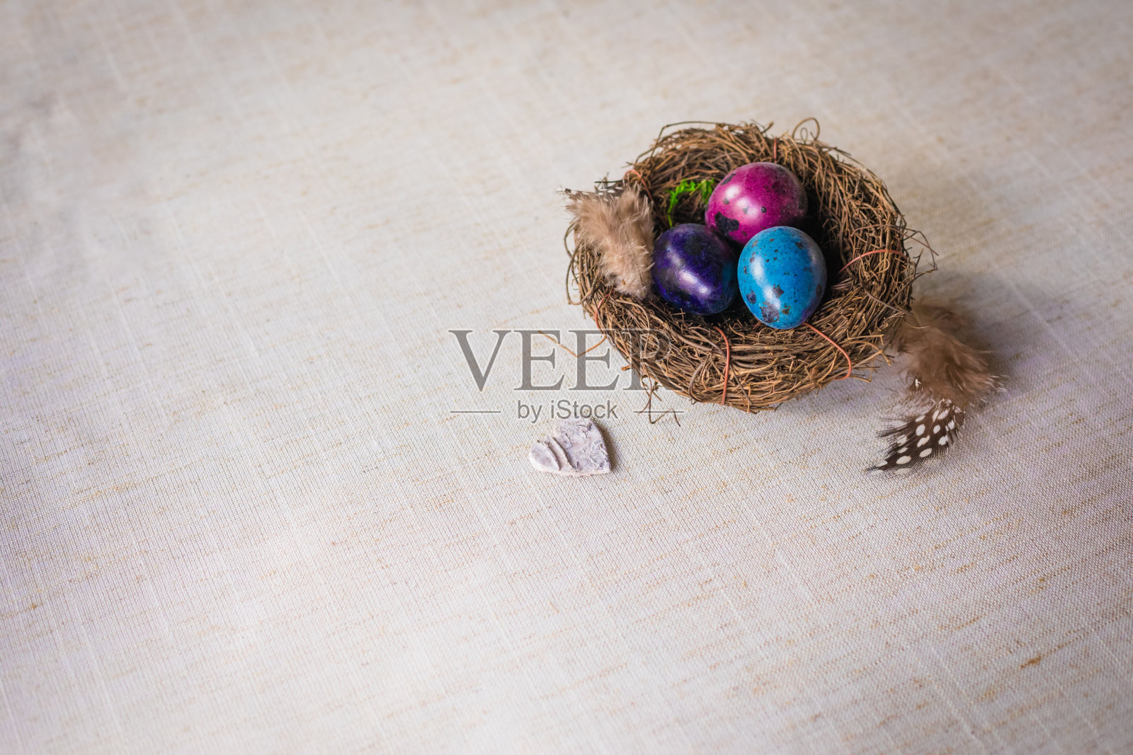 自然染色的复活节鹌鹑蛋巢与羽毛和木制心脏在亚麻的背景照片摄影图片