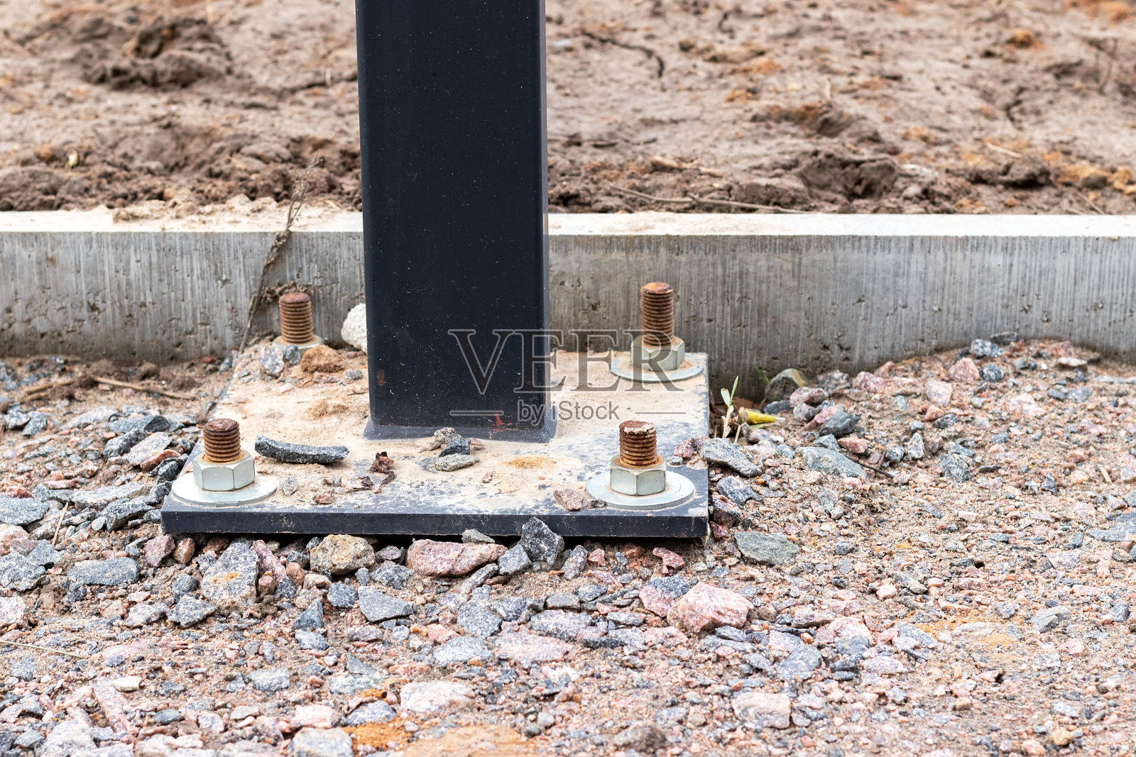 在混凝土路缘附近铺有砾石的建筑工地的轨道上安装有四个地脚螺栓的灯柱或广告牌照片摄影图片
