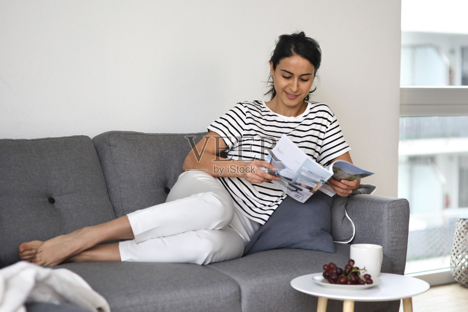 穿着休闲装的漂亮女人坐在她的沙发上消费照片摄影图片