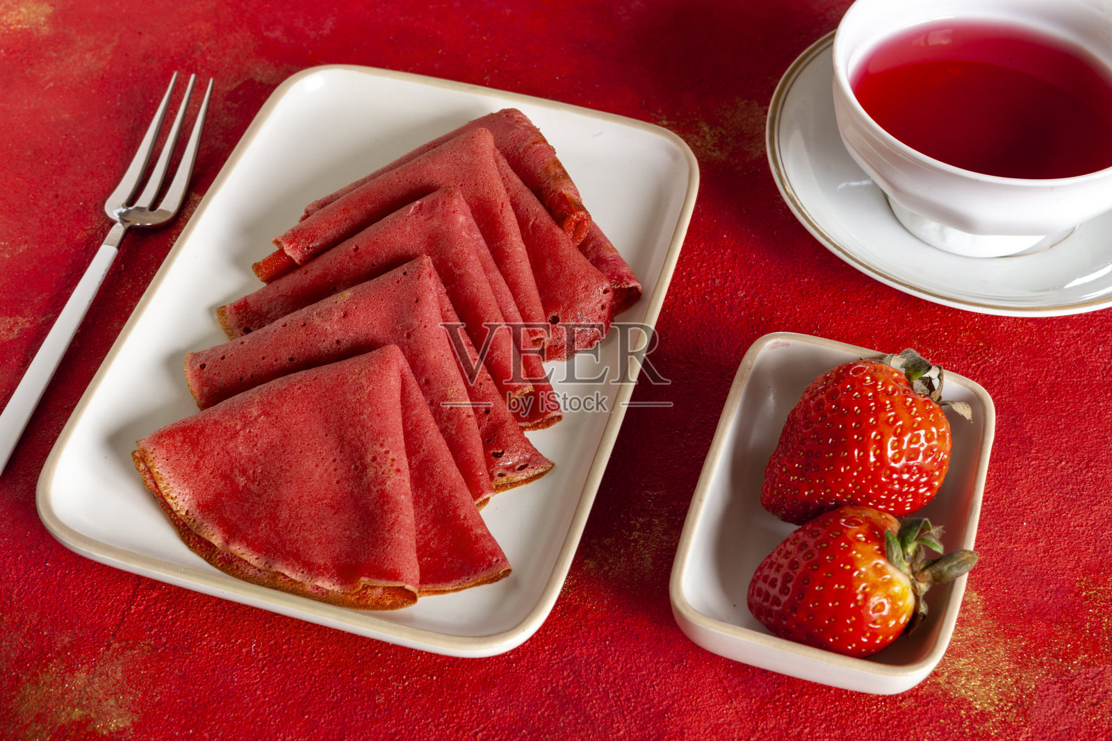 美味的自制红草莓薄煎饼，配上新鲜的草莓和红果茶。顶部视图，接近红色背景照片摄影图片