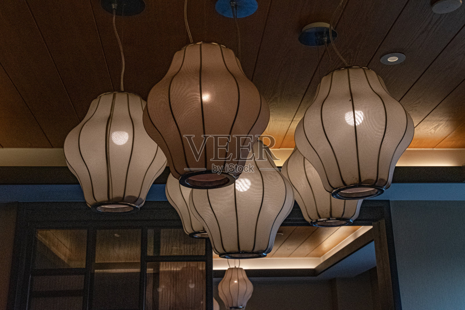 特写的复古灯与几何形状的灯罩悬挂在天花板下。米色织物表面的传统中国灯笼，发光的灯泡在里面。照片摄影图片