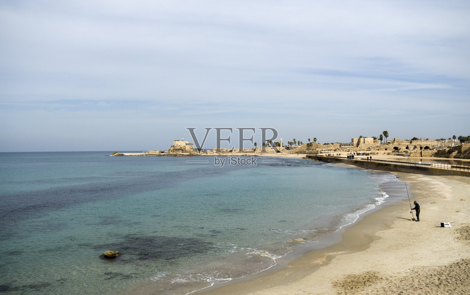 以色列凯撒利亚海湾渔民与远处港口风光照片摄影图片