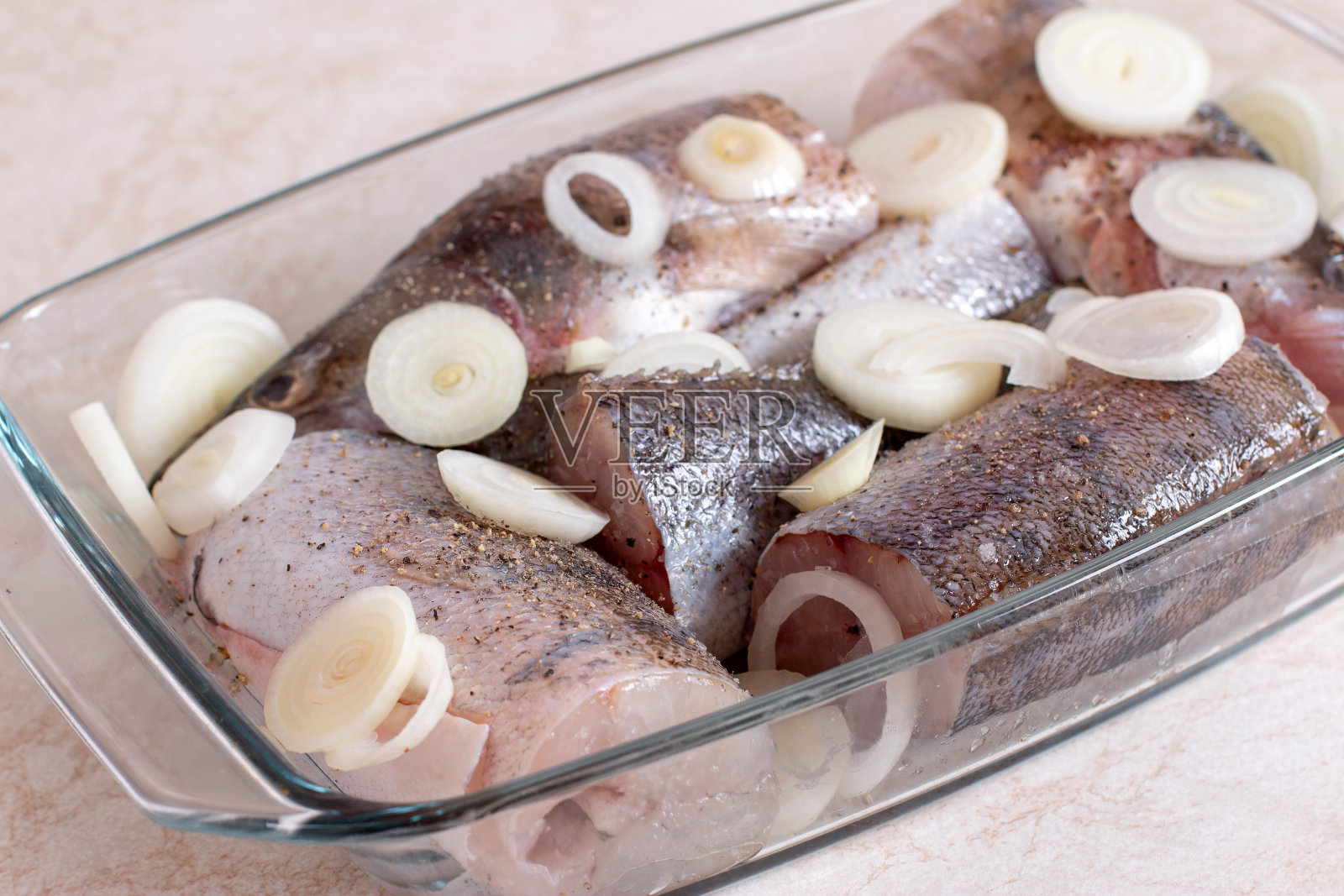 桌上的玻璃烤盘里放着生洋葱鱼照片摄影图片