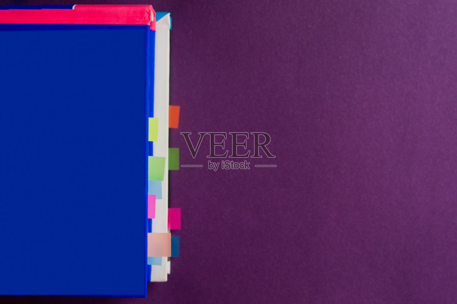 蓝色厚精装书与白色床单和蓝色书签页上紫色平滑的背景与硬阴影。照片摄影图片