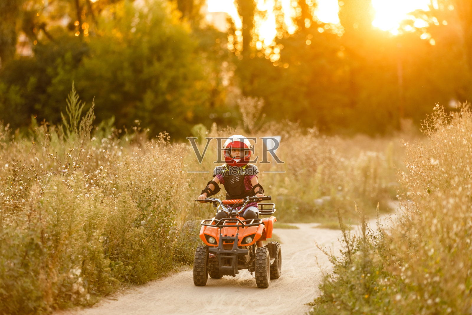 这个小女孩骑着一辆四轮沙滩车。迷你四轮摩托车是一个戴着头盔和防护服的酷女孩。儿童电动四轮自行车电动汽车，推广绿色科技。照片摄影图片