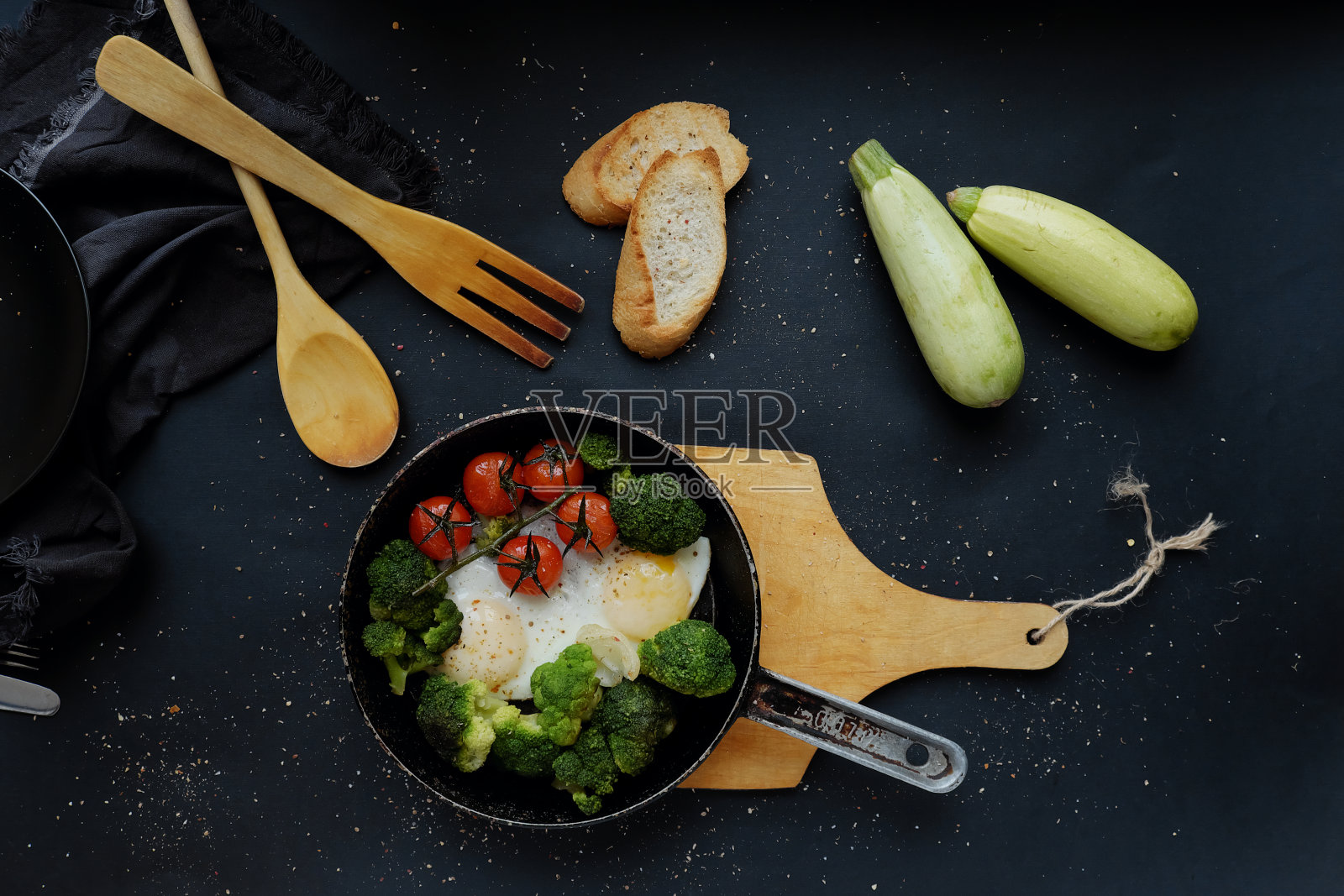 健康早餐:花椰菜、圣女果和平底煎蛋，平底煎蛋放在一个木架上，背景是黑色的。照片摄影图片