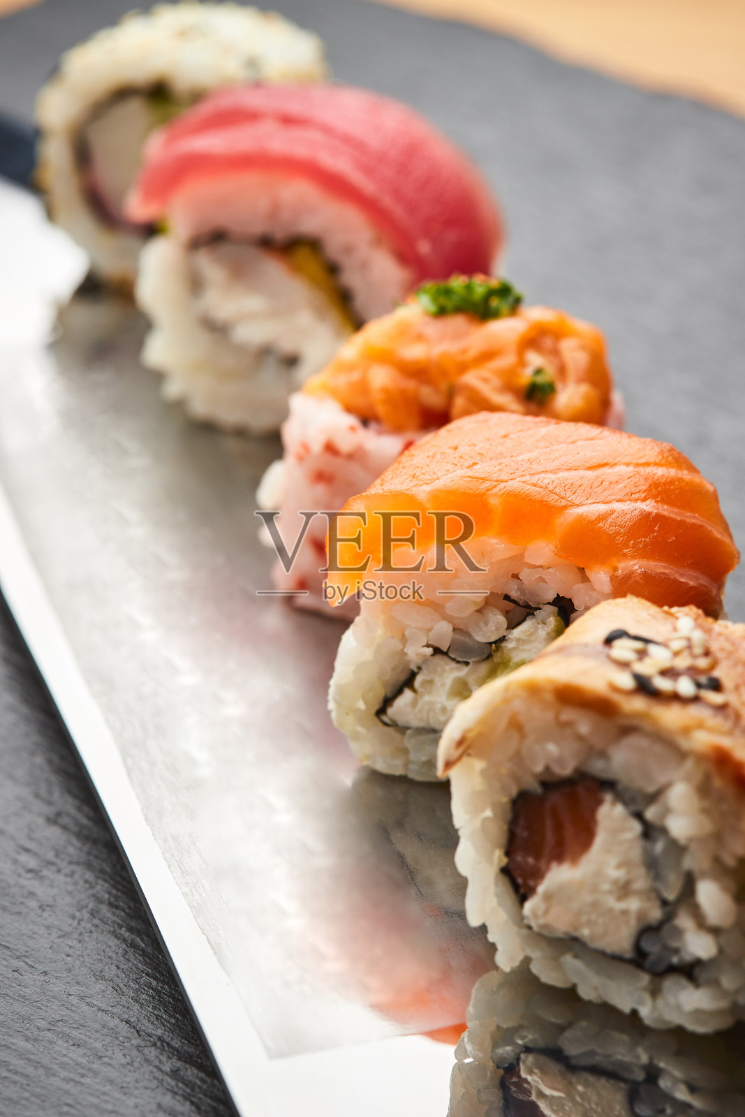 各种各样的寿司卷装在刀刃上。日本食品照片摄影图片