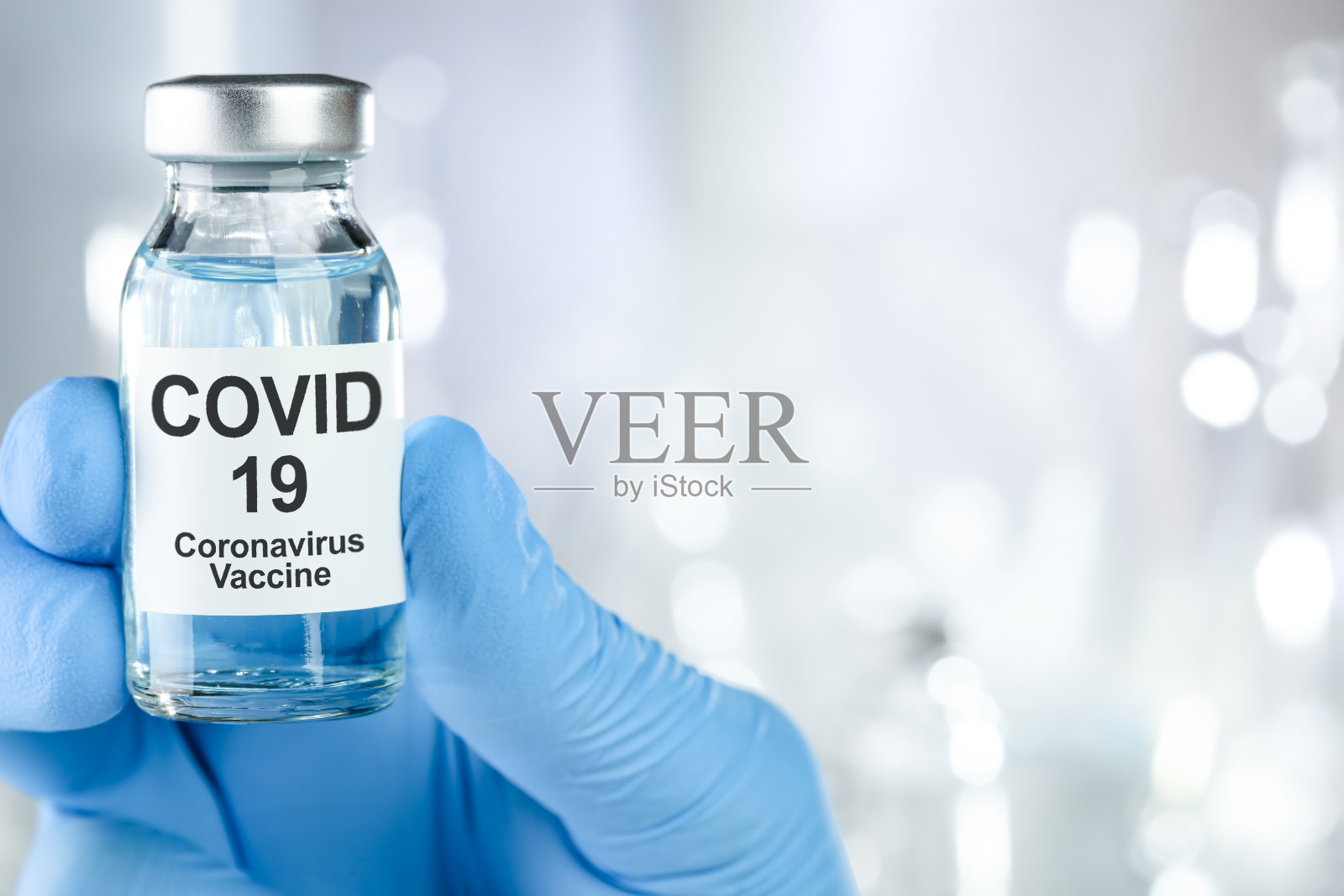 医疗救治理念用一只手拿着蓝色医用手套的冠状病毒、Covid - 19病毒、疫苗瓶照片摄影图片