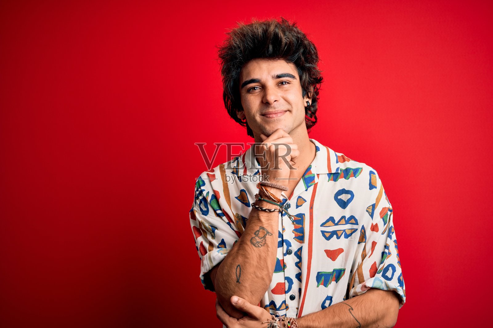 年轻英俊的男子度假穿夏天的衬衫在孤立的红色背景看起来自信在镜头微笑交叉双臂和手高举在下巴。积极的思考。照片摄影图片