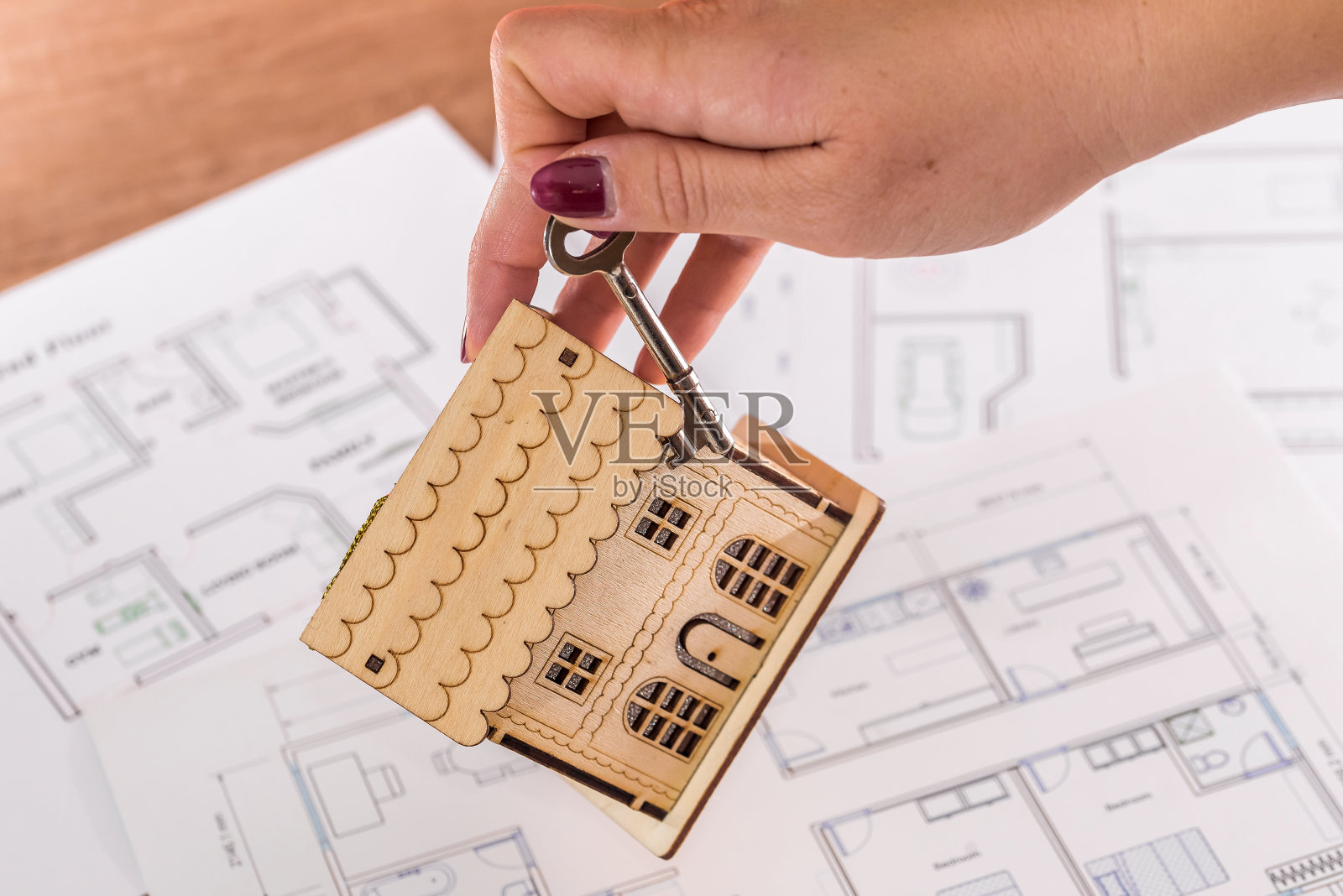 女人手拿钥匙和木制房屋模型（置于规划图上）照片摄影图片