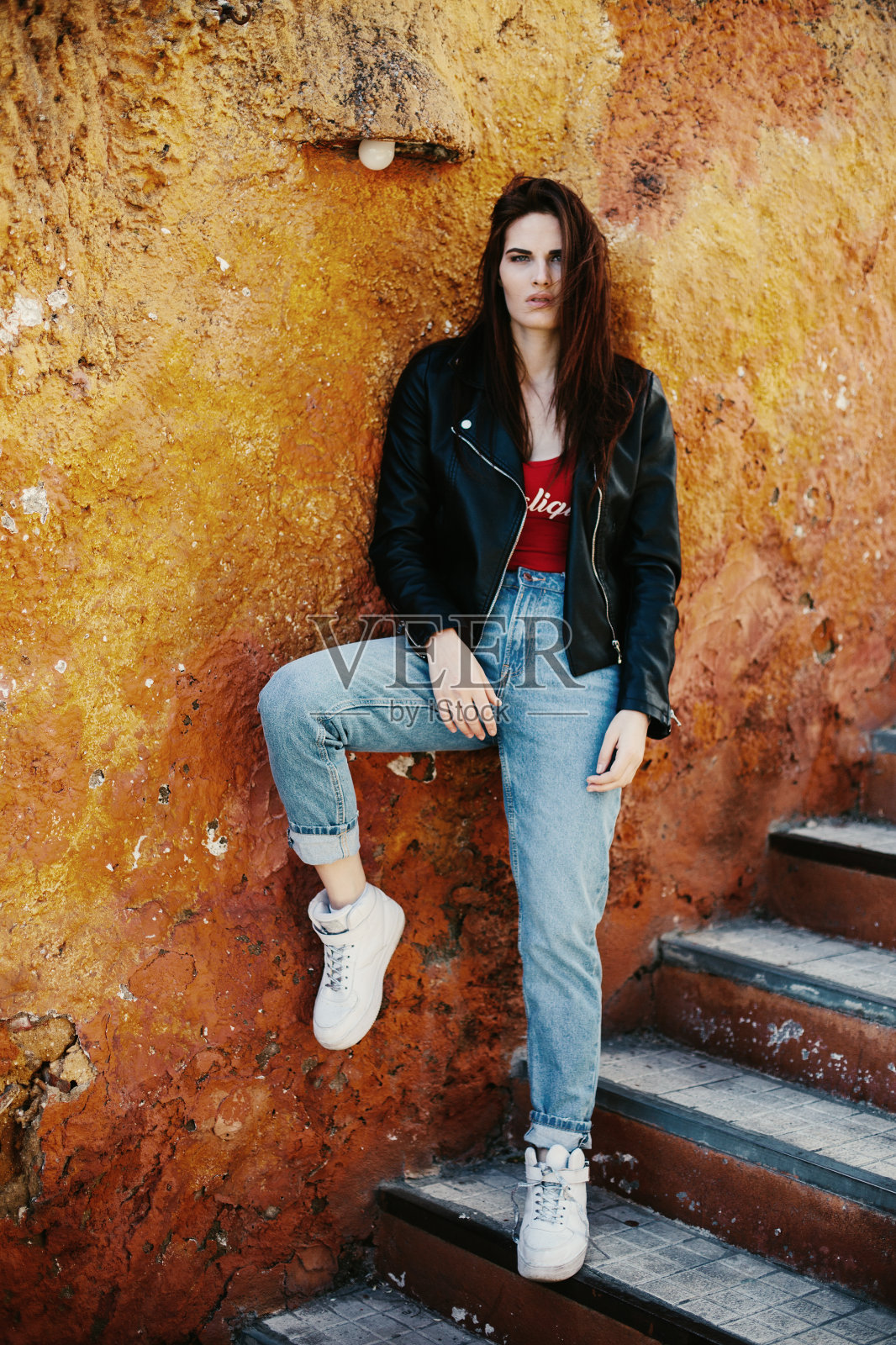 时尚女性在橙棕色墙壁附近的楼梯上照片摄影图片