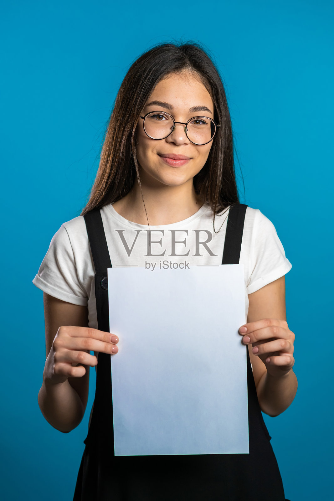 拿着白色A4纸海报的漂亮亚洲女孩，留有文案空间。在工作室背景下的留着长发的时髦微笑女性照片摄影图片