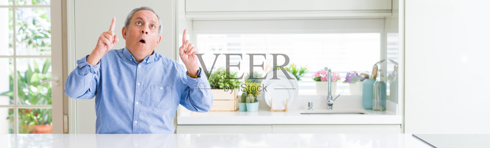 在家中惊讶地向上看并用手指和手臂指着的年长男人的广角照片照片摄影图片