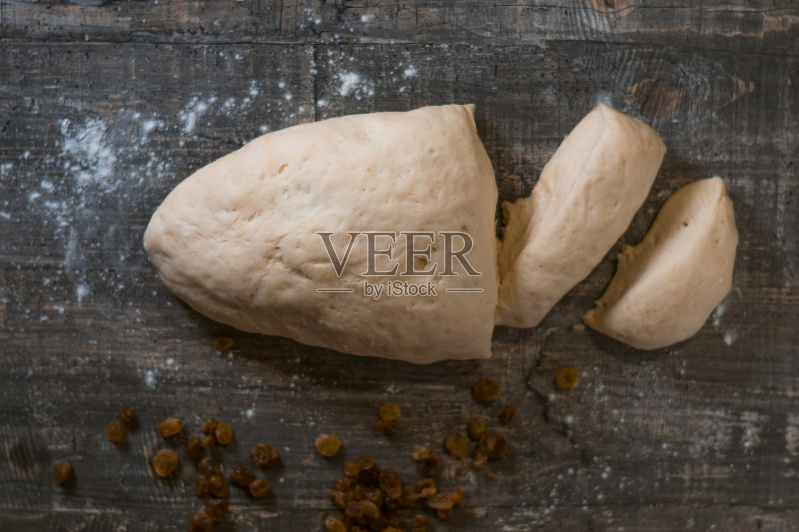 新鲜的自制面团和葡萄干片放在木桌上。小麦粉撒在桌子上。制作馅饼的过程。照片摄影图片