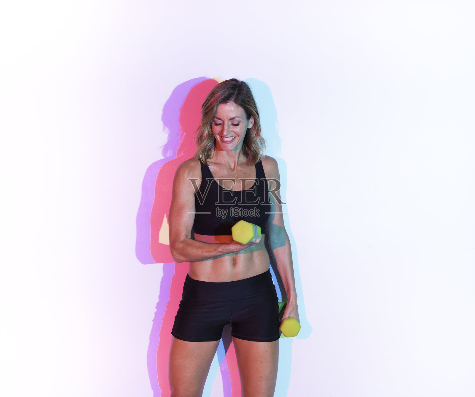 白人女子在彩色背景前运动，身穿运动服进行负重训练照片摄影图片