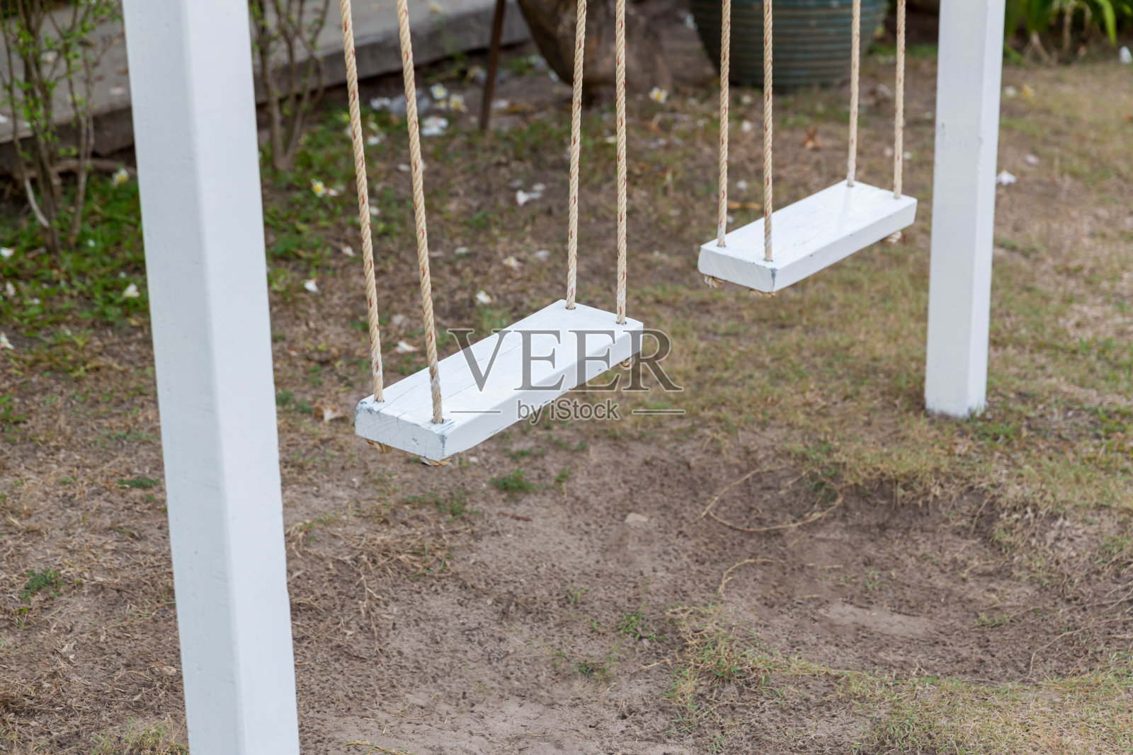 旧的木秋千悬挂在地面下面。儿童游乐场的秋千挂在公园的花园里。以自然为背景的花卉花园中空白的白色木制秋千。照片摄影图片