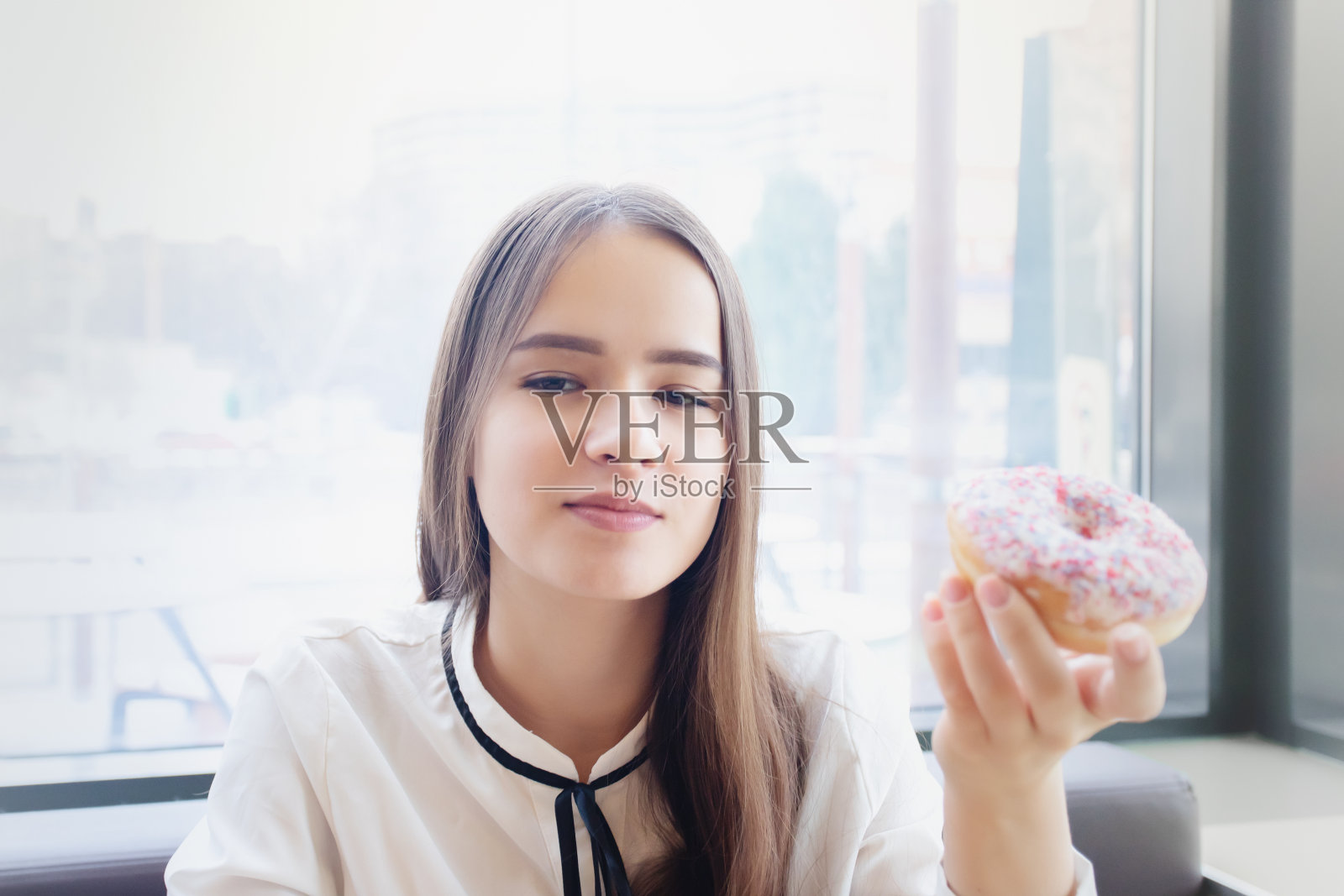 漂亮的女孩在咖啡馆的桌旁拿着美味的甜甜圈照片摄影图片