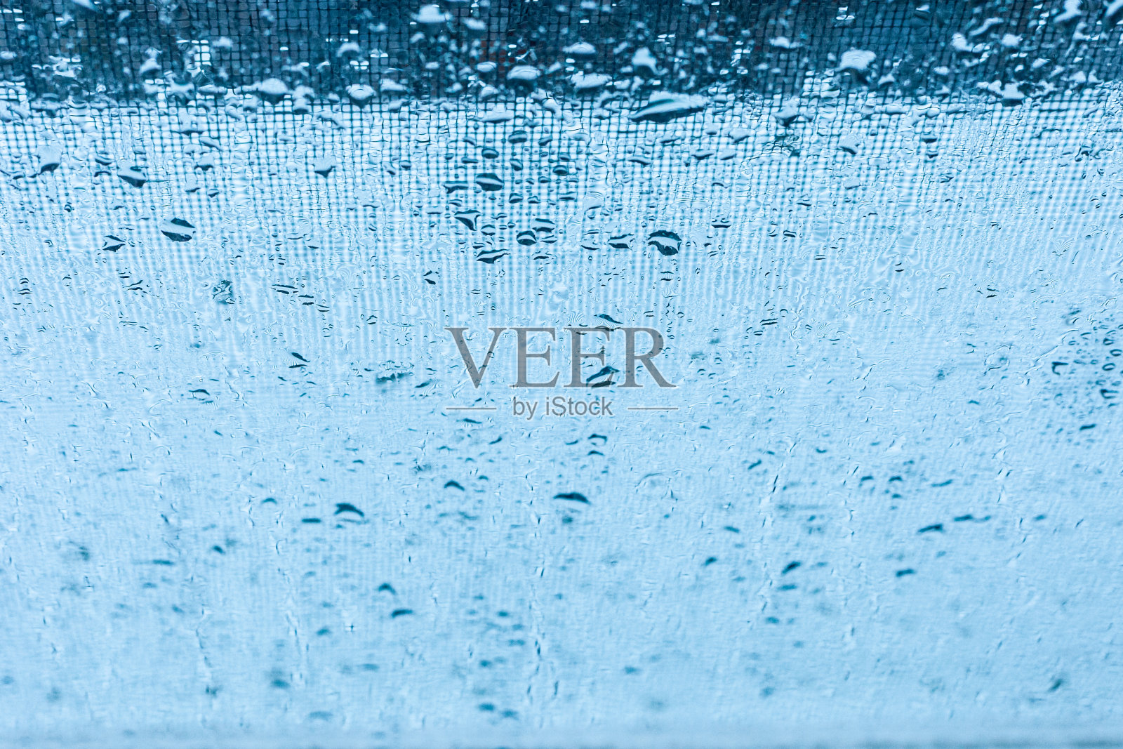 蓝色窗玻璃上的雨滴与模糊的溪流和网格抽象的背景。照片摄影图片