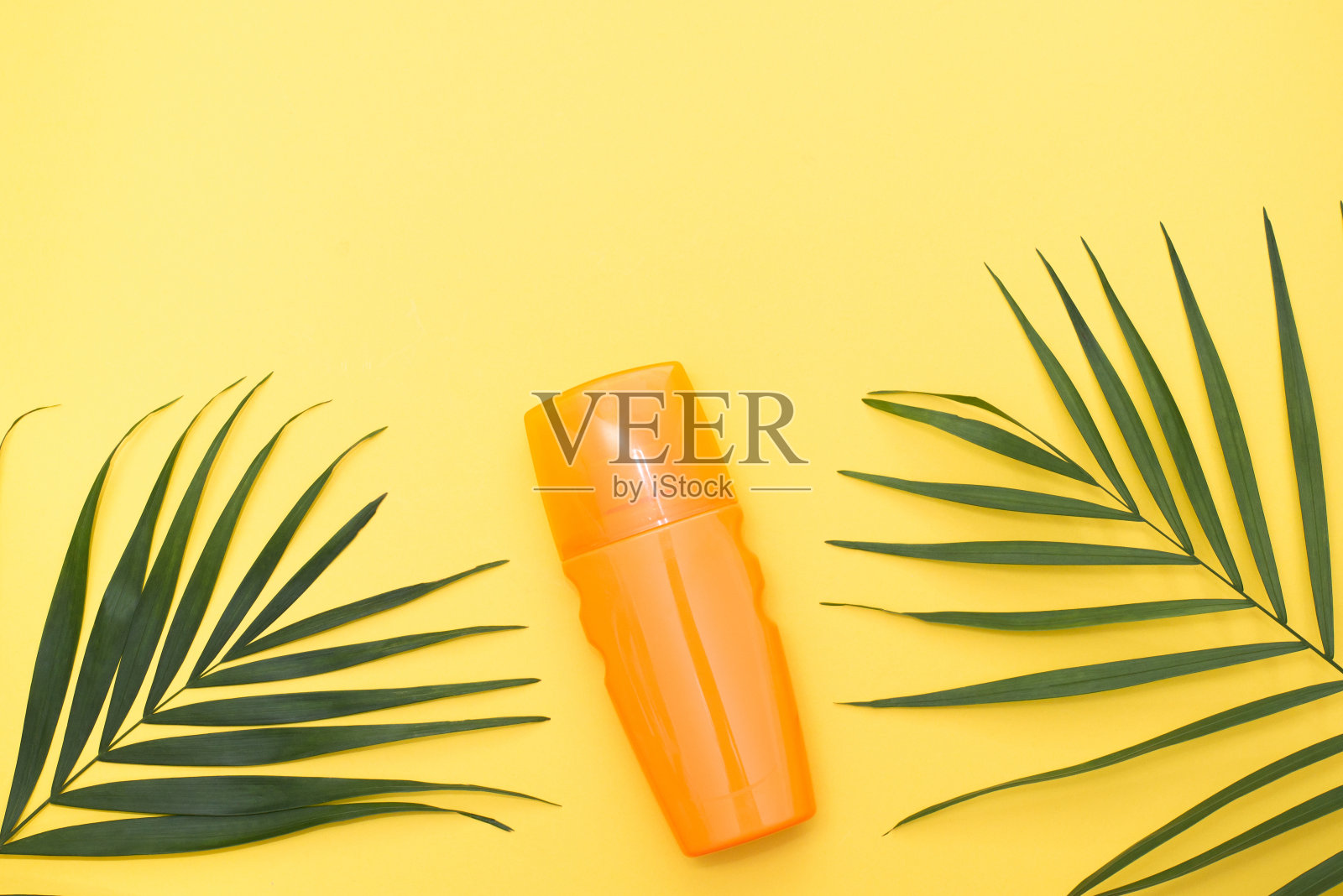一瓶防晒霜，黄色背景和绿色植物照片摄影图片