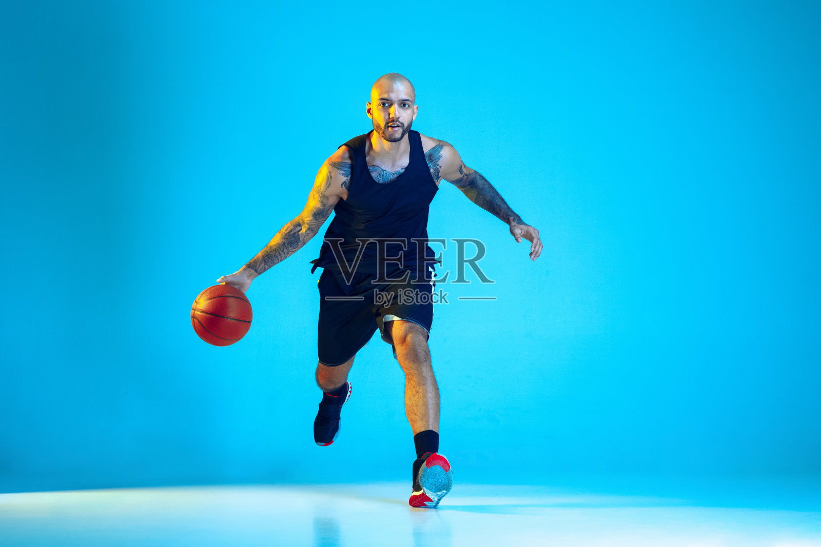 在蓝色演播室霓虹灯背景下训练的年轻篮球运动员照片摄影图片