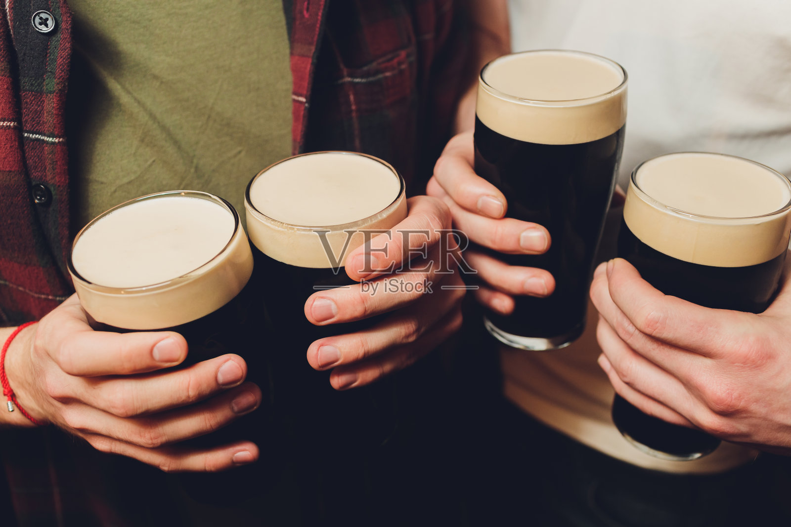 在砖墙背景上碰杯深色和浅色啤酒的一群男人照片摄影图片