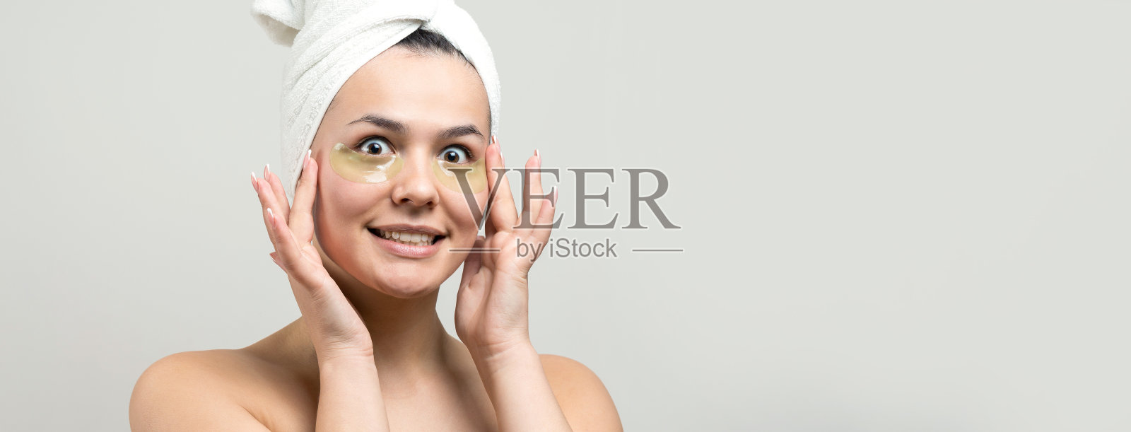 年轻美丽的女孩在一个白色的毛巾在他的头上戴着胶原凝胶眼罩。敷眼罩治疗面部。照片摄影图片