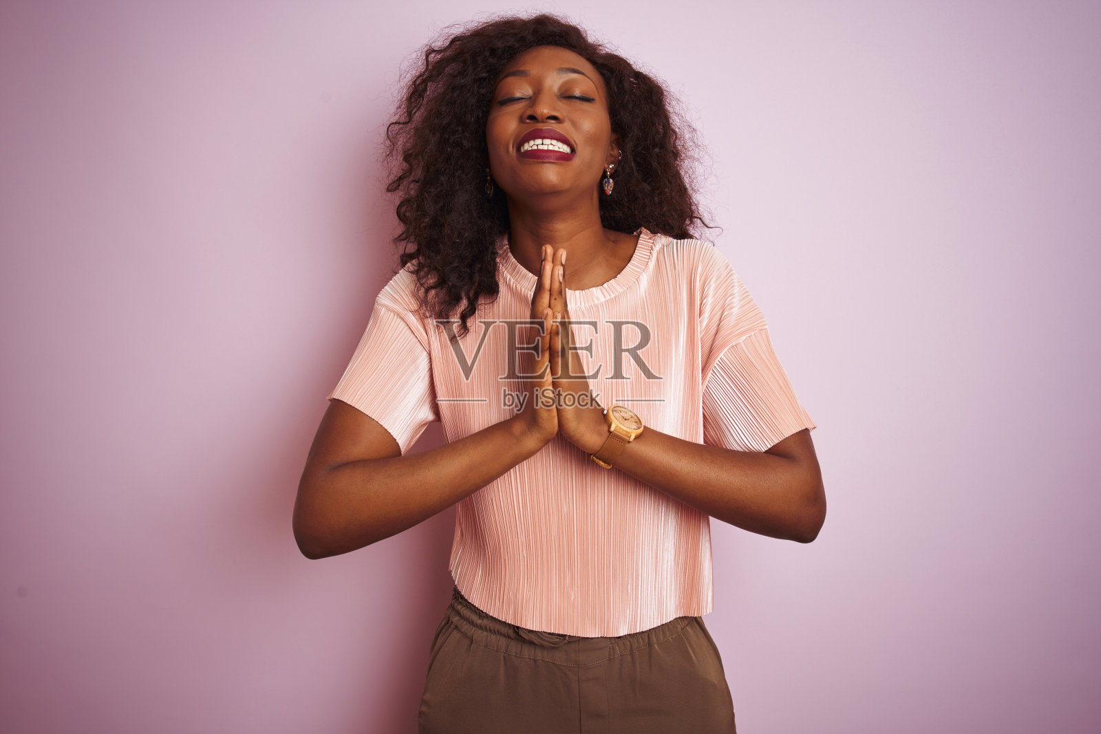 年轻的非洲裔美国妇女穿着t恤站在孤立的粉红色背景乞求和祈祷手在一起的希望表情非常激动和担心。请求宽恕。宗教的概念。照片摄影图片