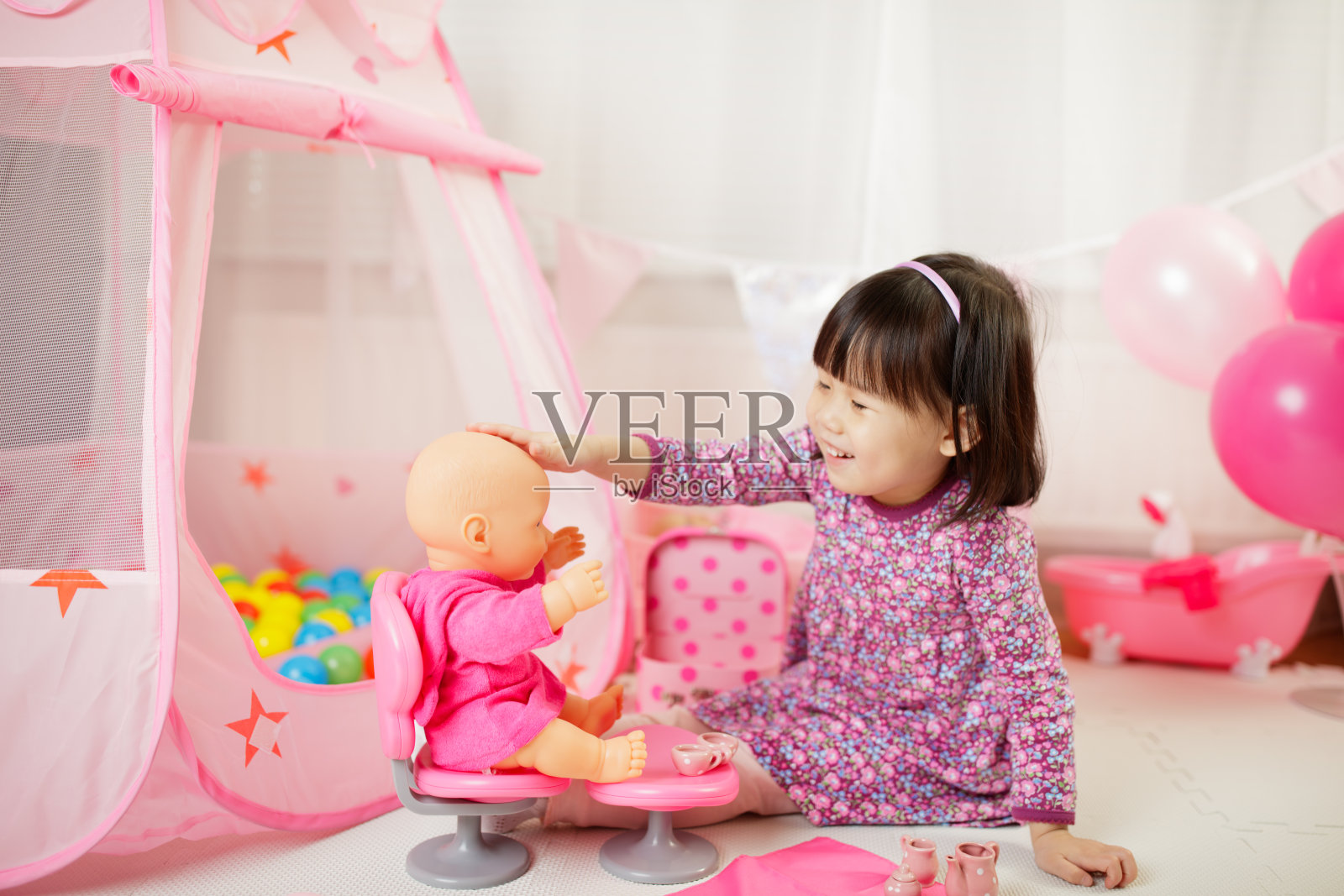 蹒跚学步的女孩在白色背景下在家假装玩婴儿护理照片摄影图片