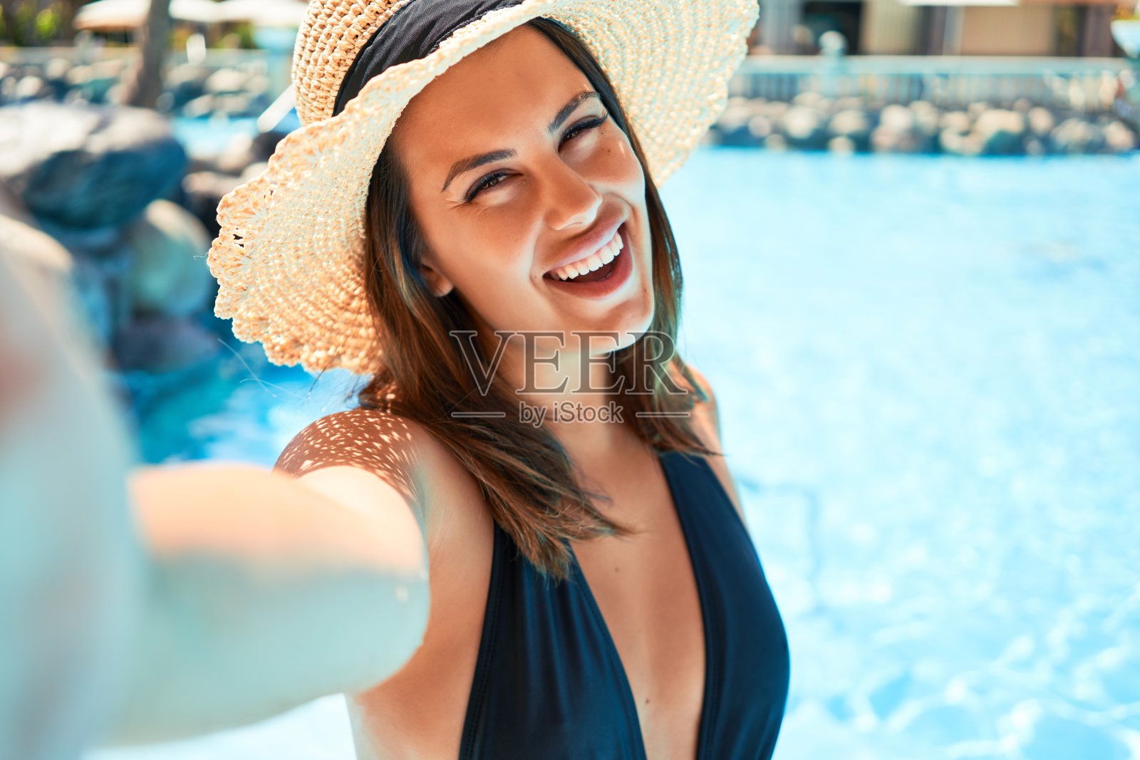 年轻美丽和性感的女人在酒店游泳池用智能手机自拍在阳光明媚的日子照片摄影图片